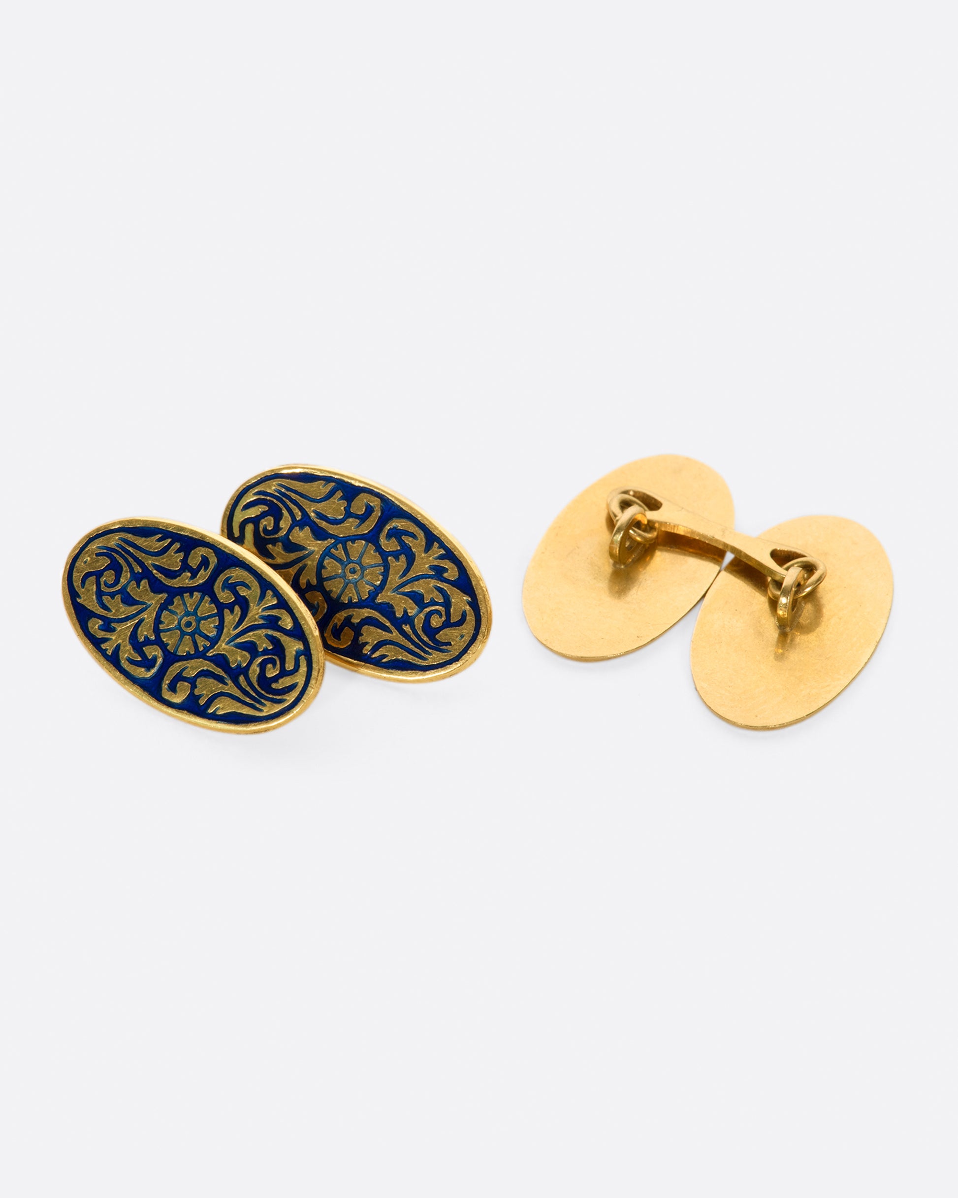 A pair of solid gold vintage cufflinks with intricate flourishes and contrasting dark blue enamel.