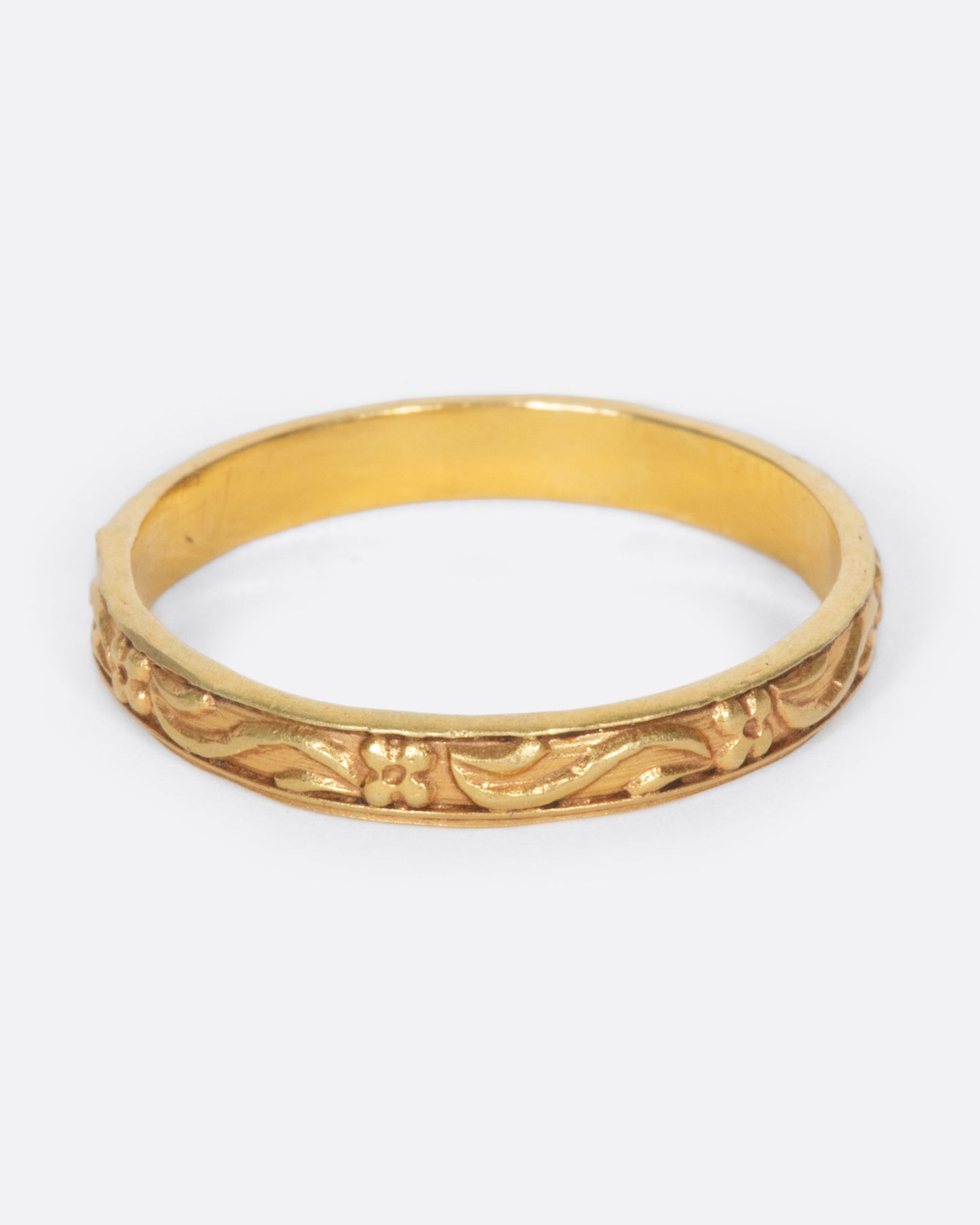 A vintage yellow gold narrow band ring with flowers and leaves throughout.