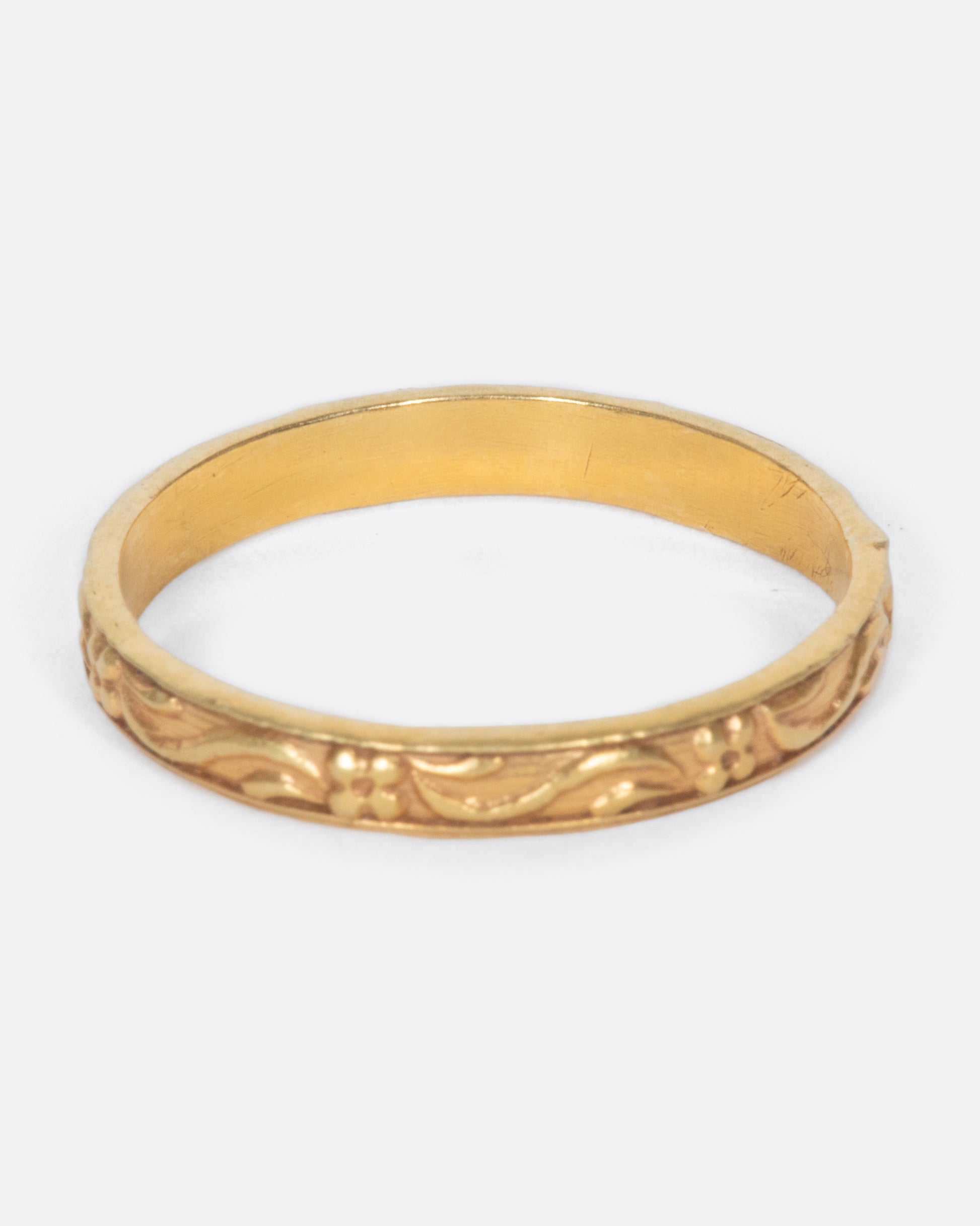 A vintage yellow gold narrow band ring with flowers and leaves throughout.