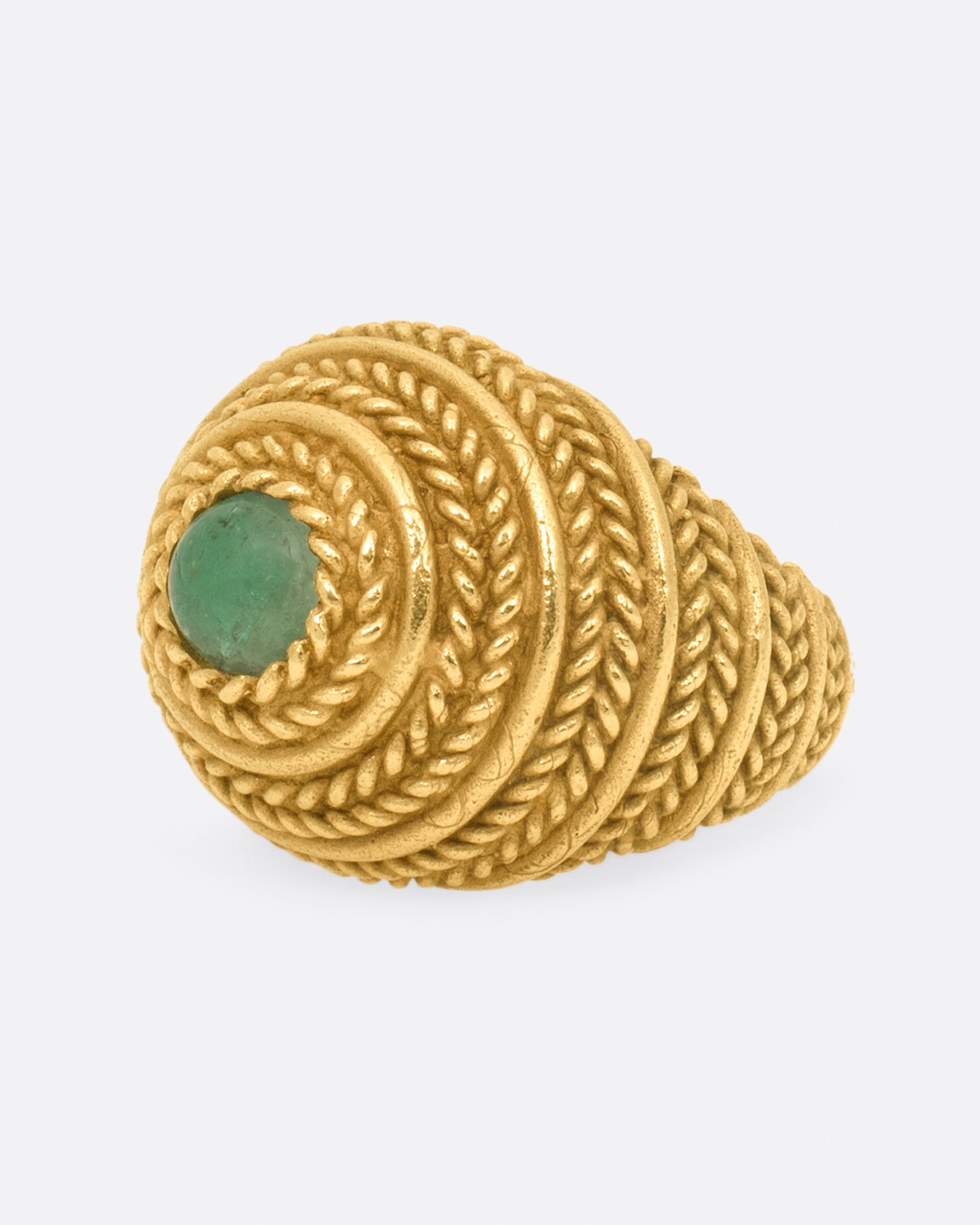 A dome ring covered in braided texture with an emerald cabochon at its peak.