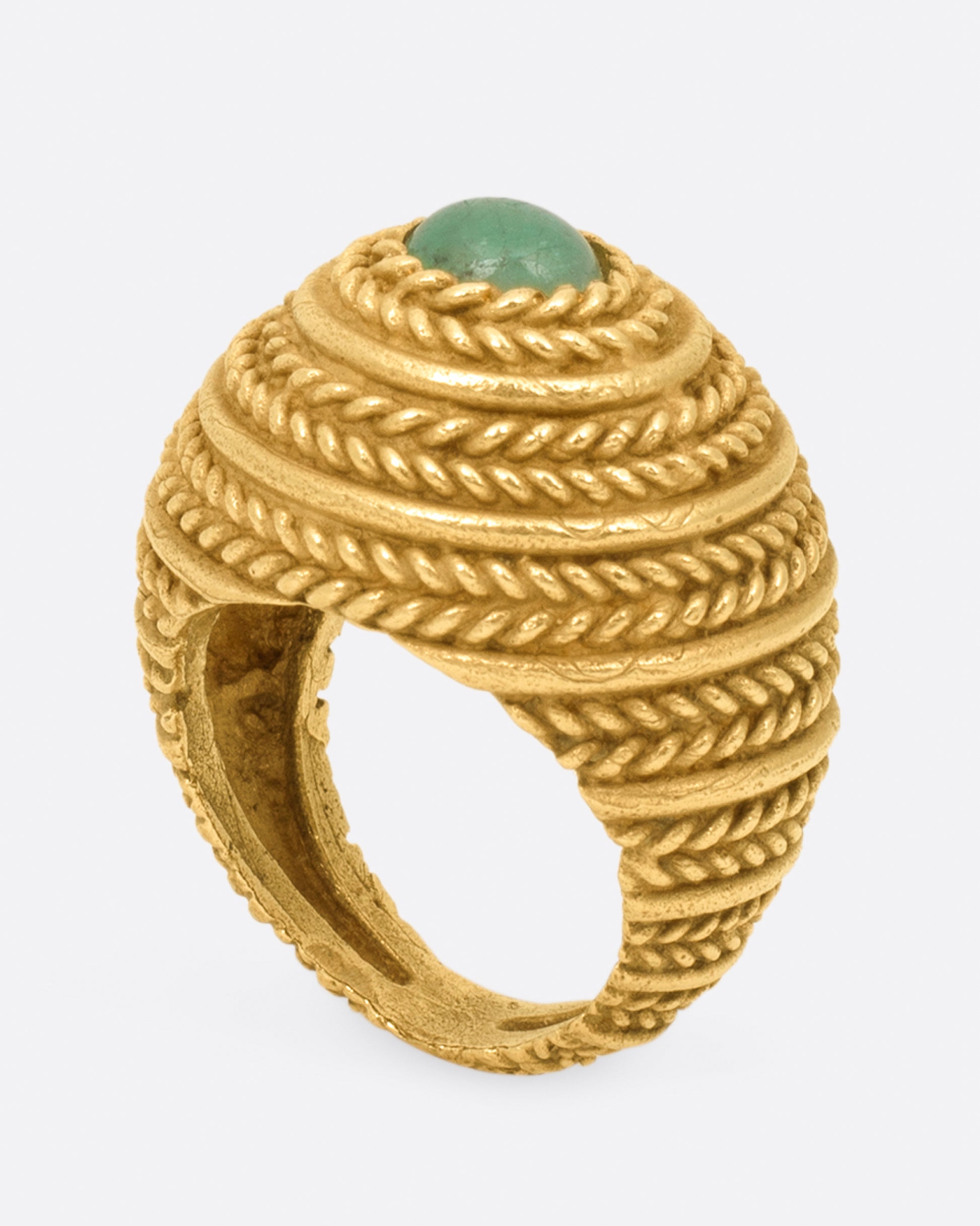 A dome ring covered in braided texture with an emerald cabochon at its peak.