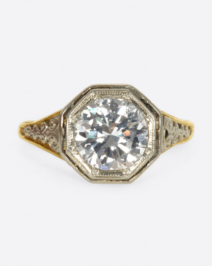Vintage ring in yellow and white gold, a round diamond in an octagonal white gold bezel on an openwork filigree shank