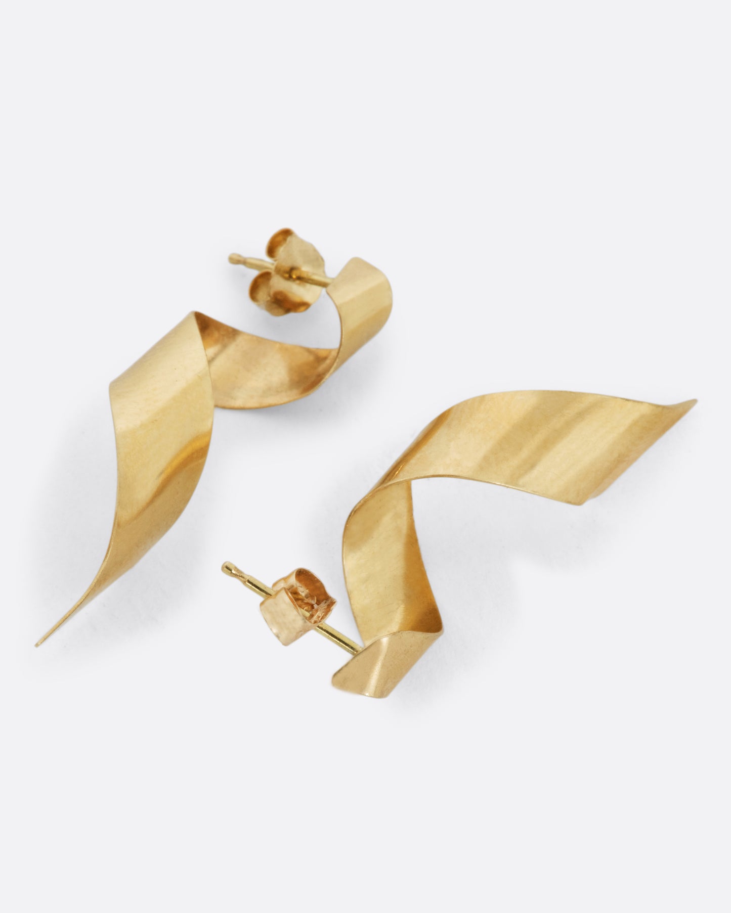 A pair of drop earrings made from 3D swirled gold ribbons. Shown from the side.