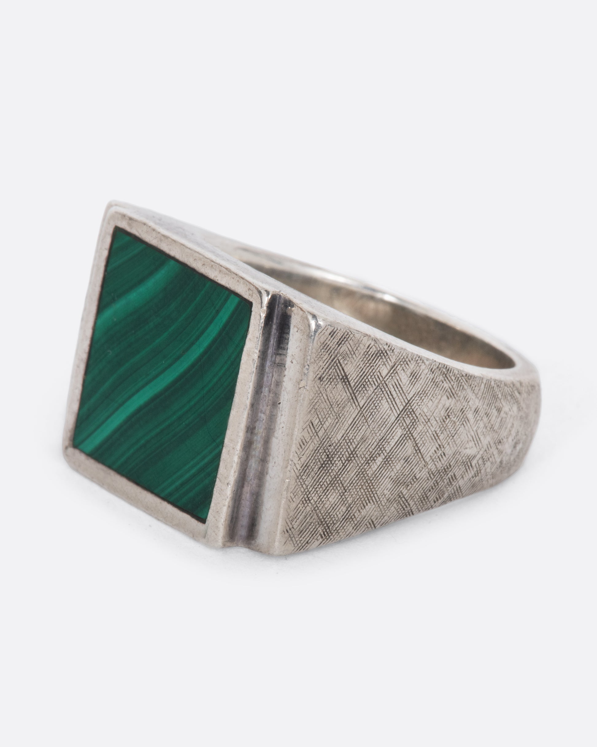 A vintage sterling silver signet ring with a large square malachite at its center, stepped sides, and a wide textured band. Shown from the side.