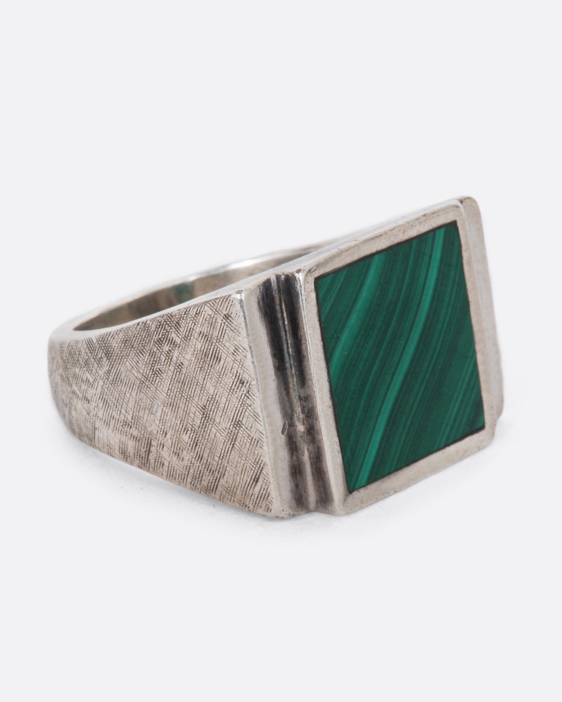 A vintage sterling silver signet ring with a large square malachite at its center, stepped sides, and a wide textured band. Shown from the side.