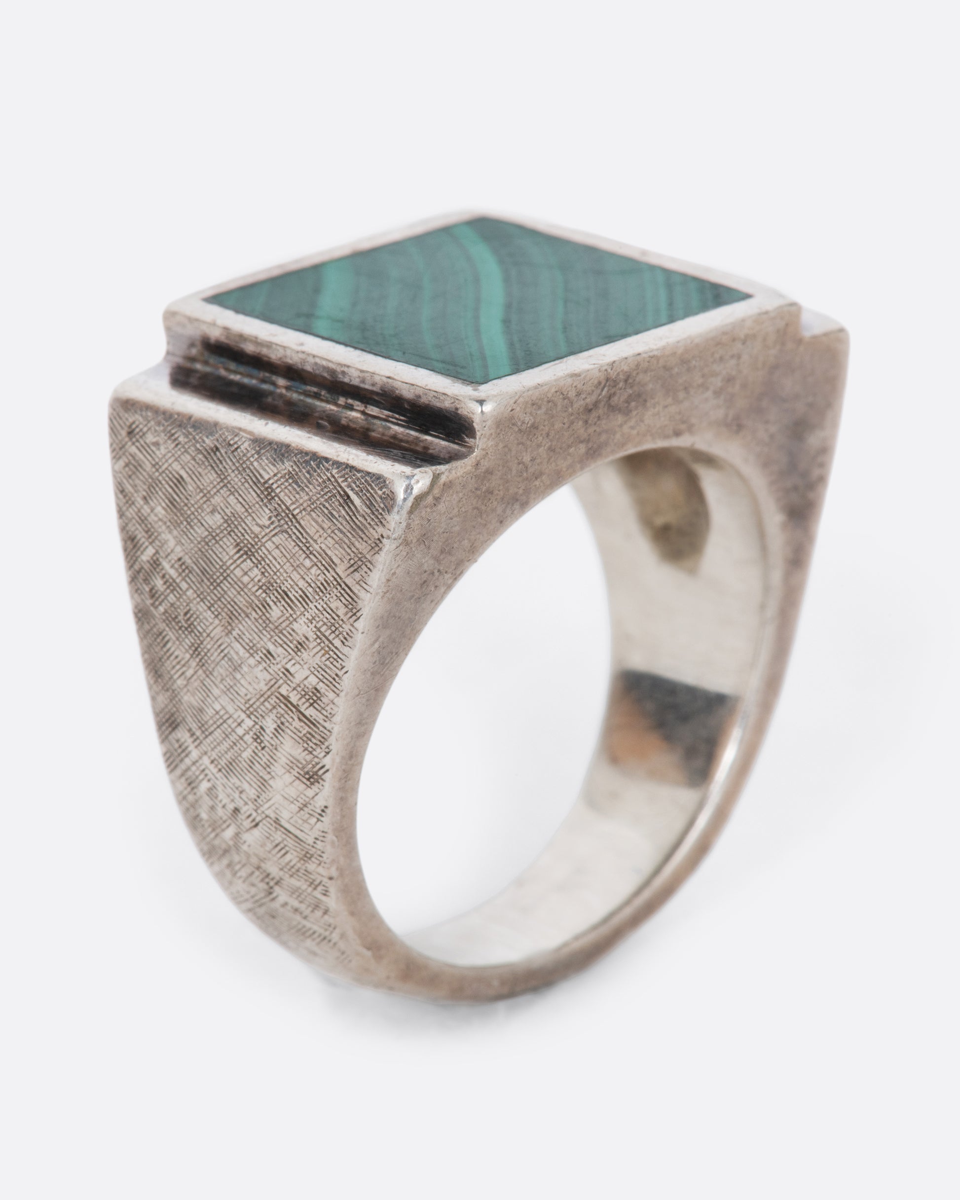 A vintage sterling silver signet ring with a large square malachite at its center, stepped sides, and a wide textured band. Shown from the side.