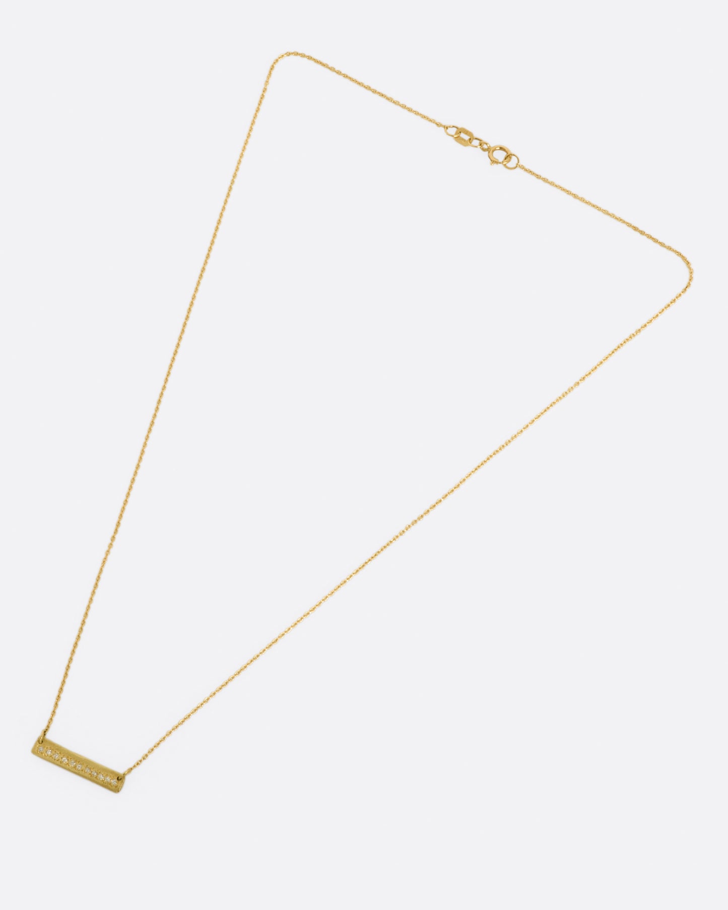 A yellow gold bar necklace with a single row of white diamonds. View on the entire necklace, laying flat.