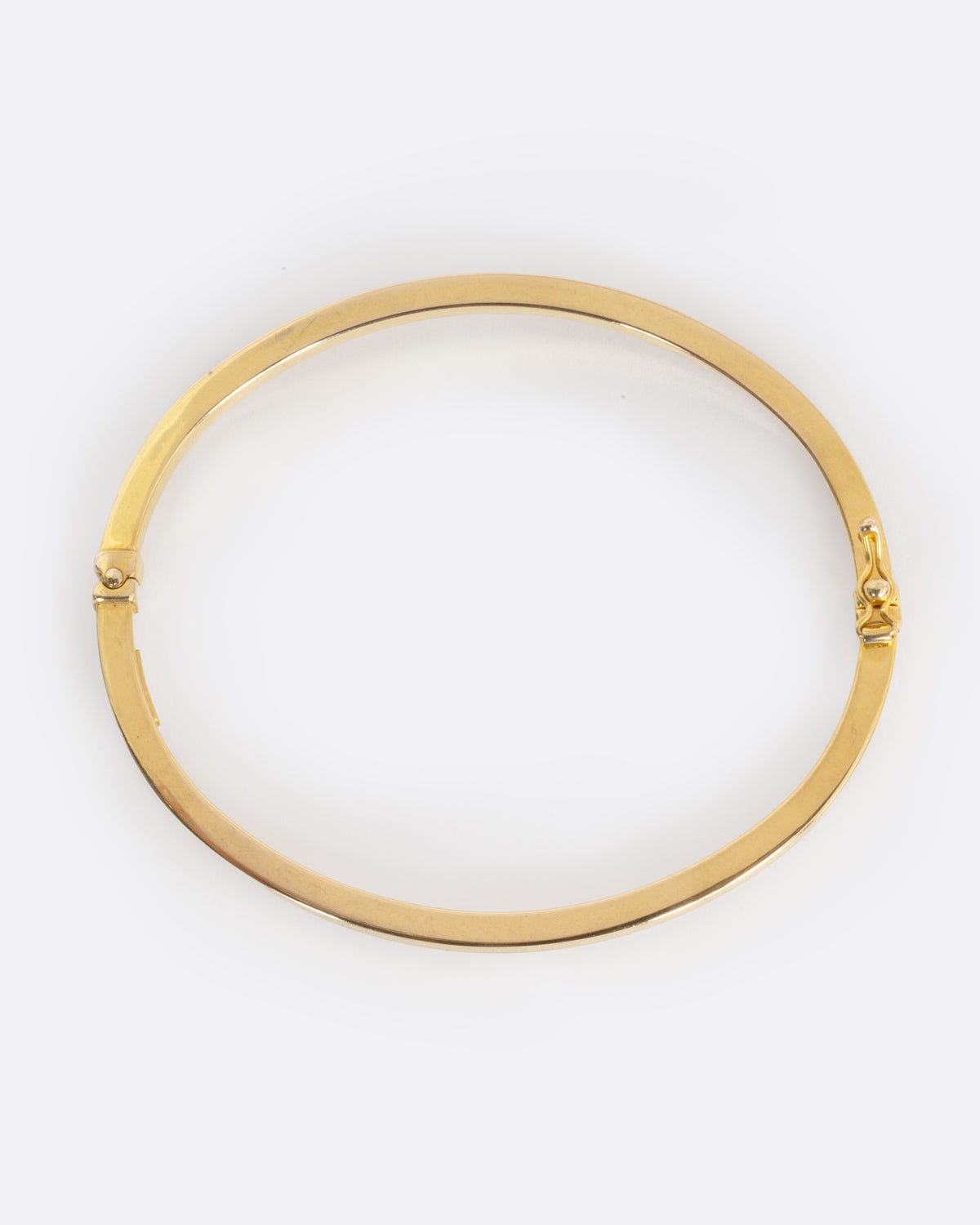A yellow gold oval hinged bangle with a security clasp, shown from from above laying flat.