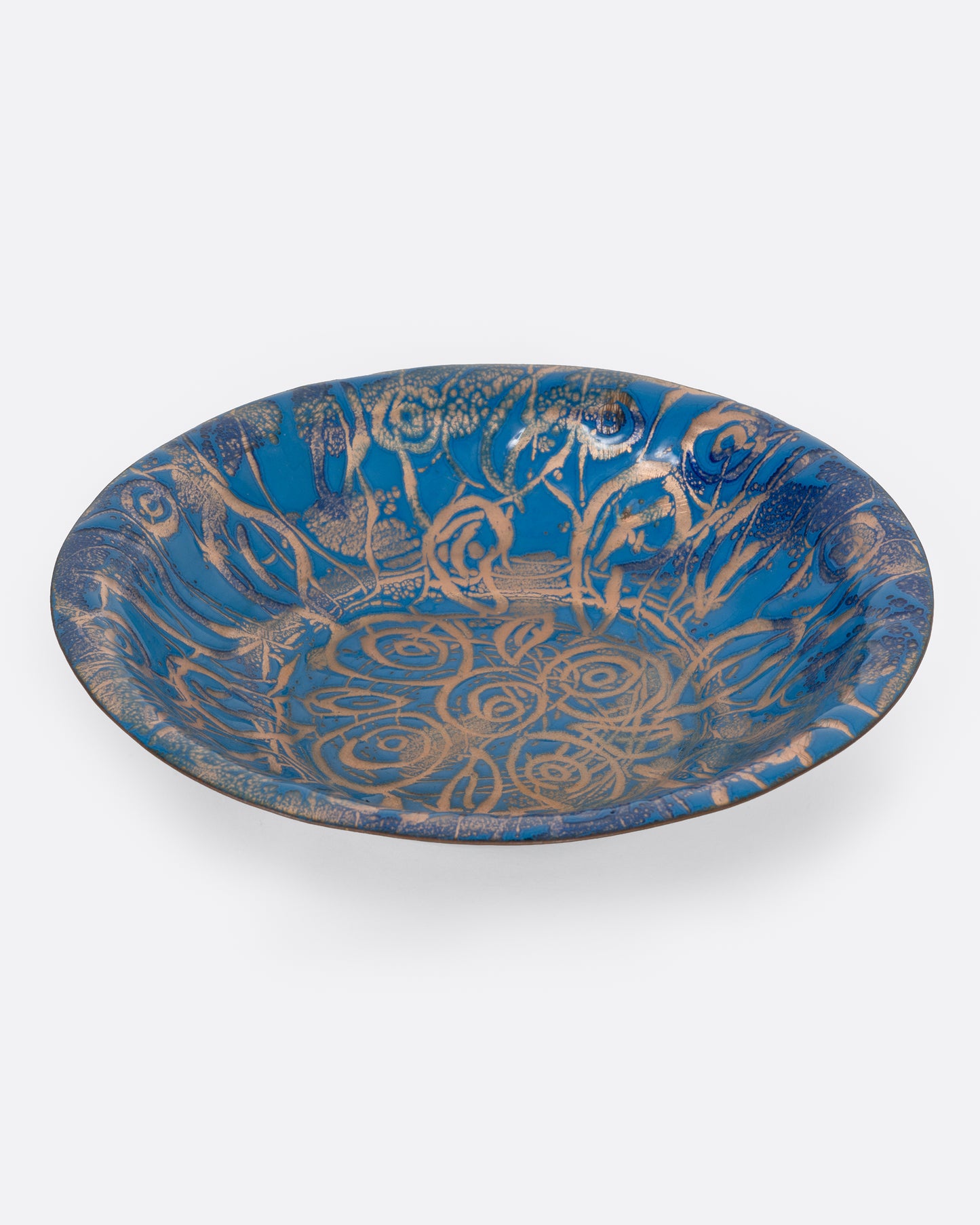 A blue enamel plate with a network of gold swirls, shown from the side.