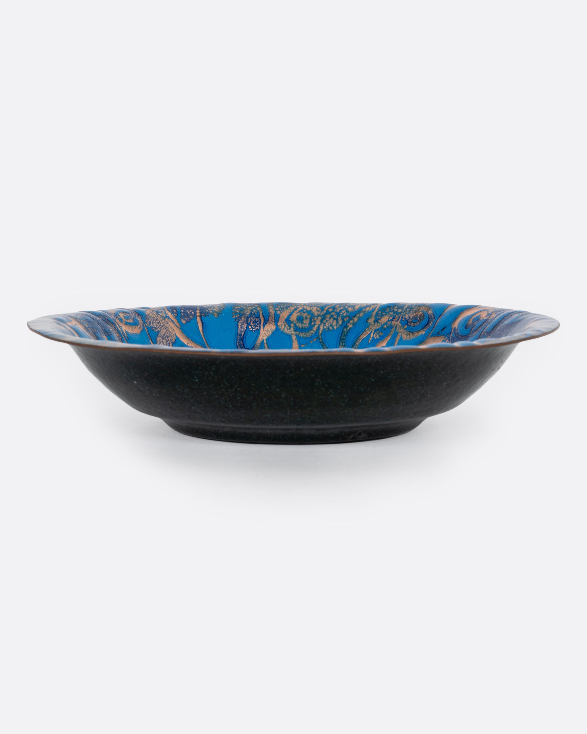 A blue enamel plate with a network of gold swirls, shown from the side.