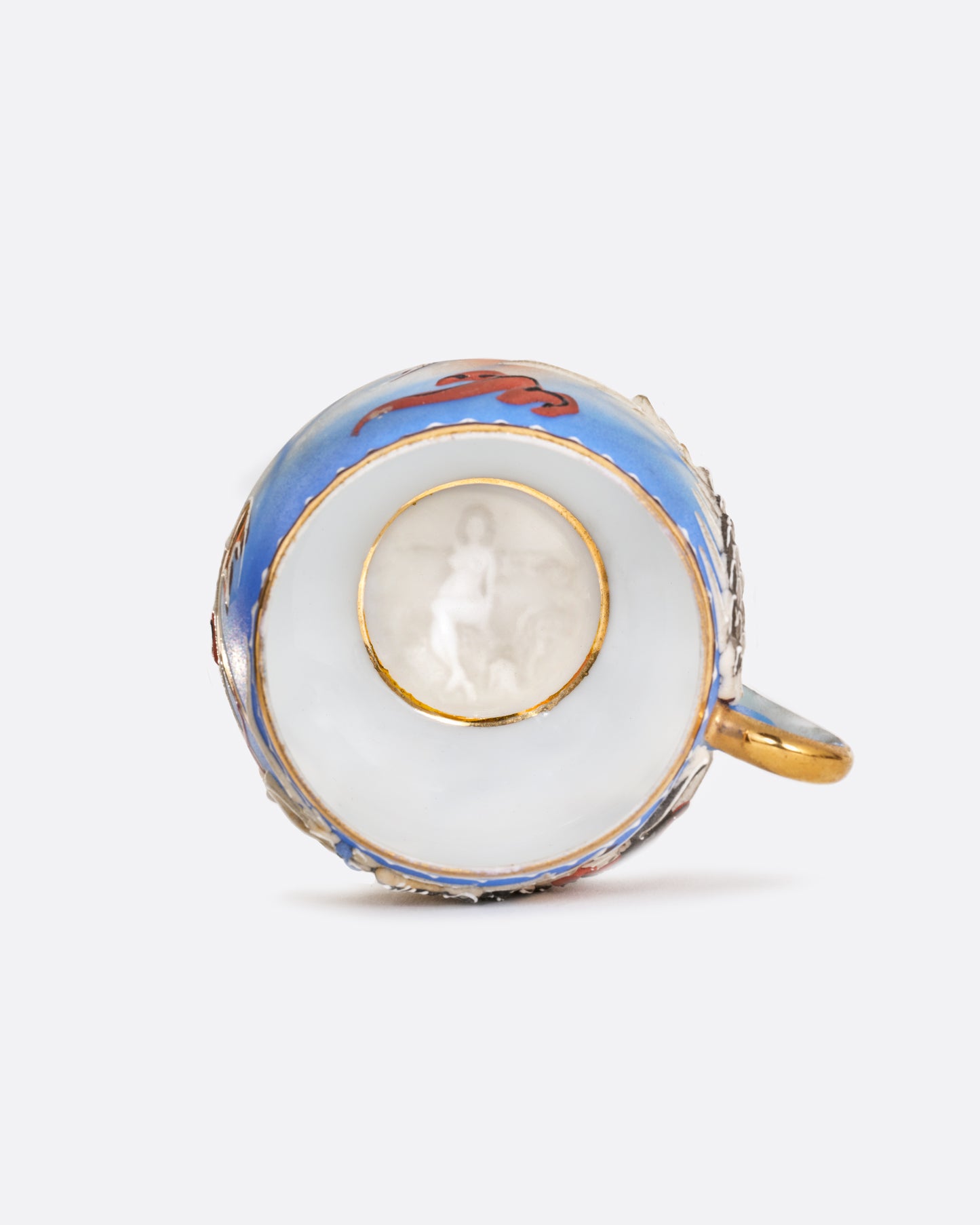 A dragonware moriage teacup and saucer with an enamel dragon motif in vibrant hues. A lithophane nude figure sits at the base of the cup. Shown from the top.