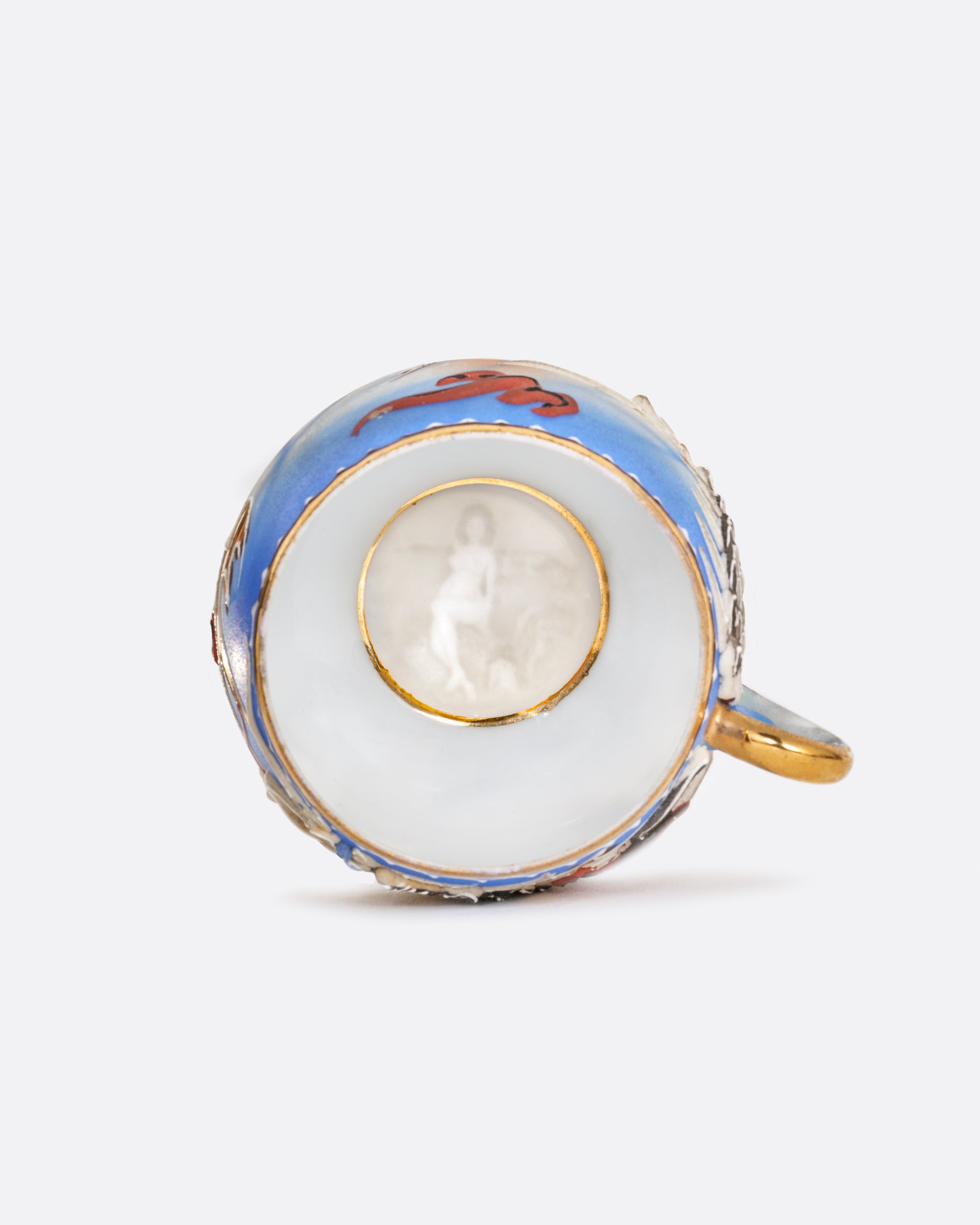 A dragonware moriage teacup and saucer with an enamel dragon motif in vibrant hues. A lithophane nude figure sits at the base of the cup. Shown from the top.