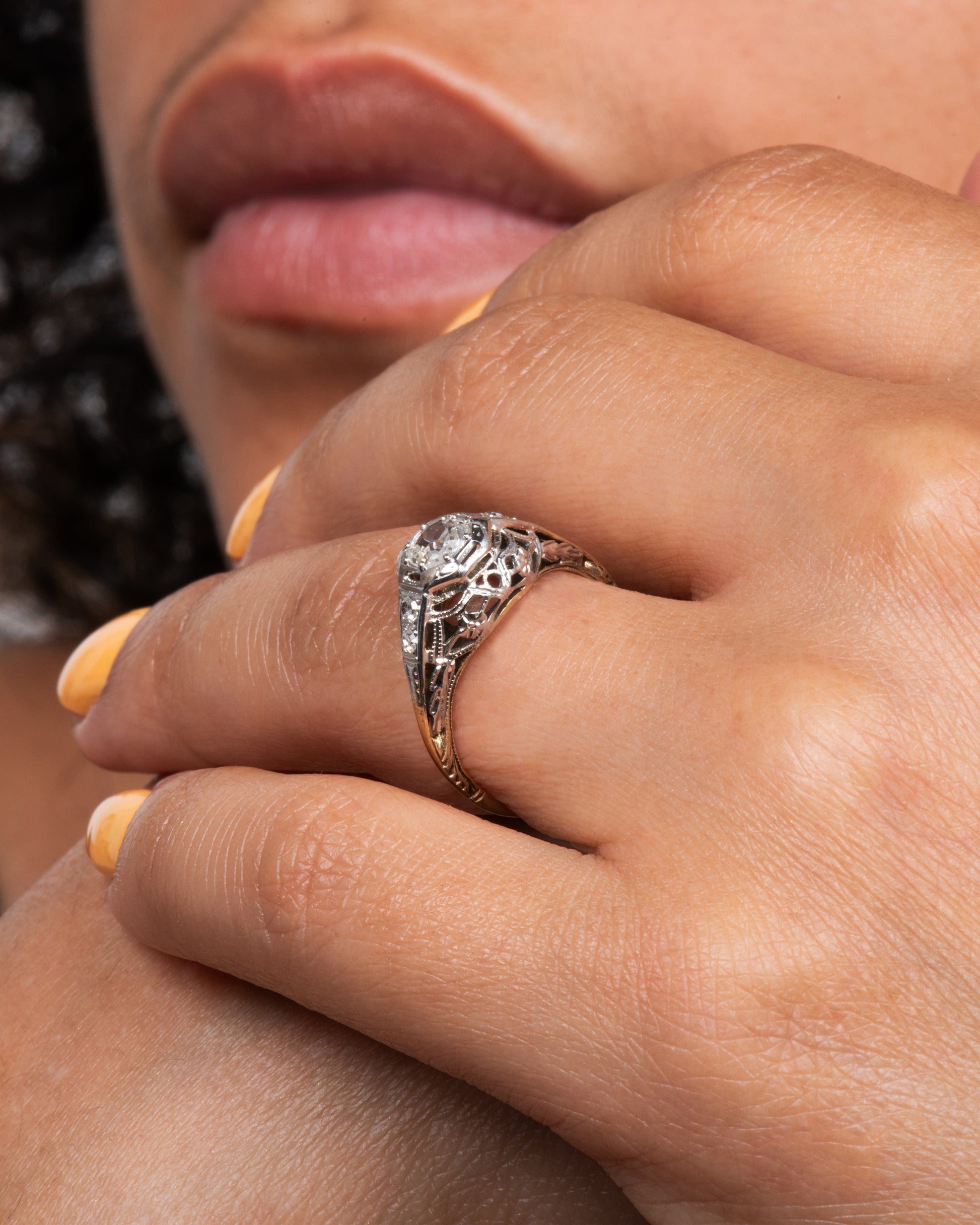 A white gold filigree ring with old mine cut center diamond and a yellow gold band. View on hand.