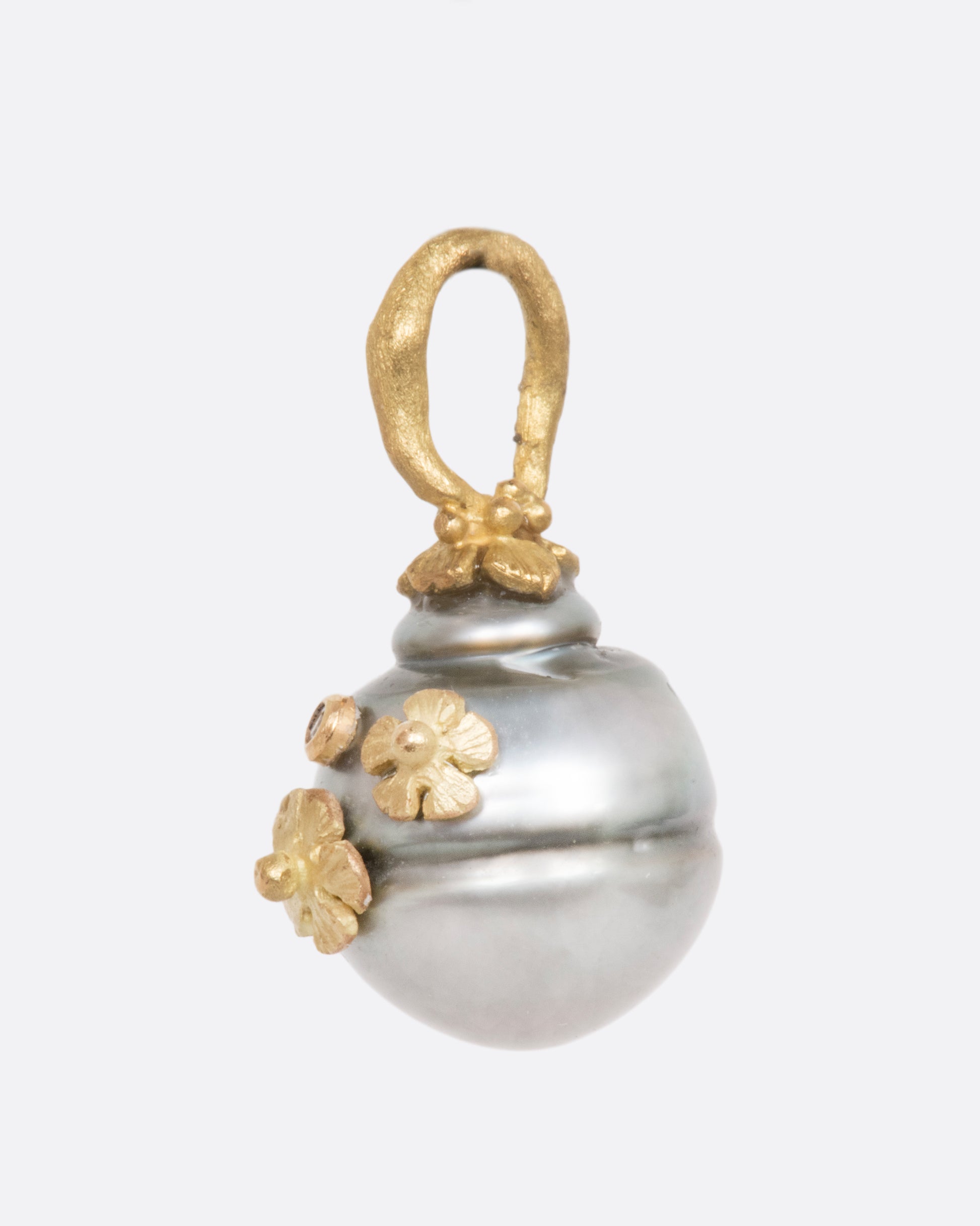 A pearl pendant with a yellow gold bale, adorned with tiny flowers and a diamond. View from the side.