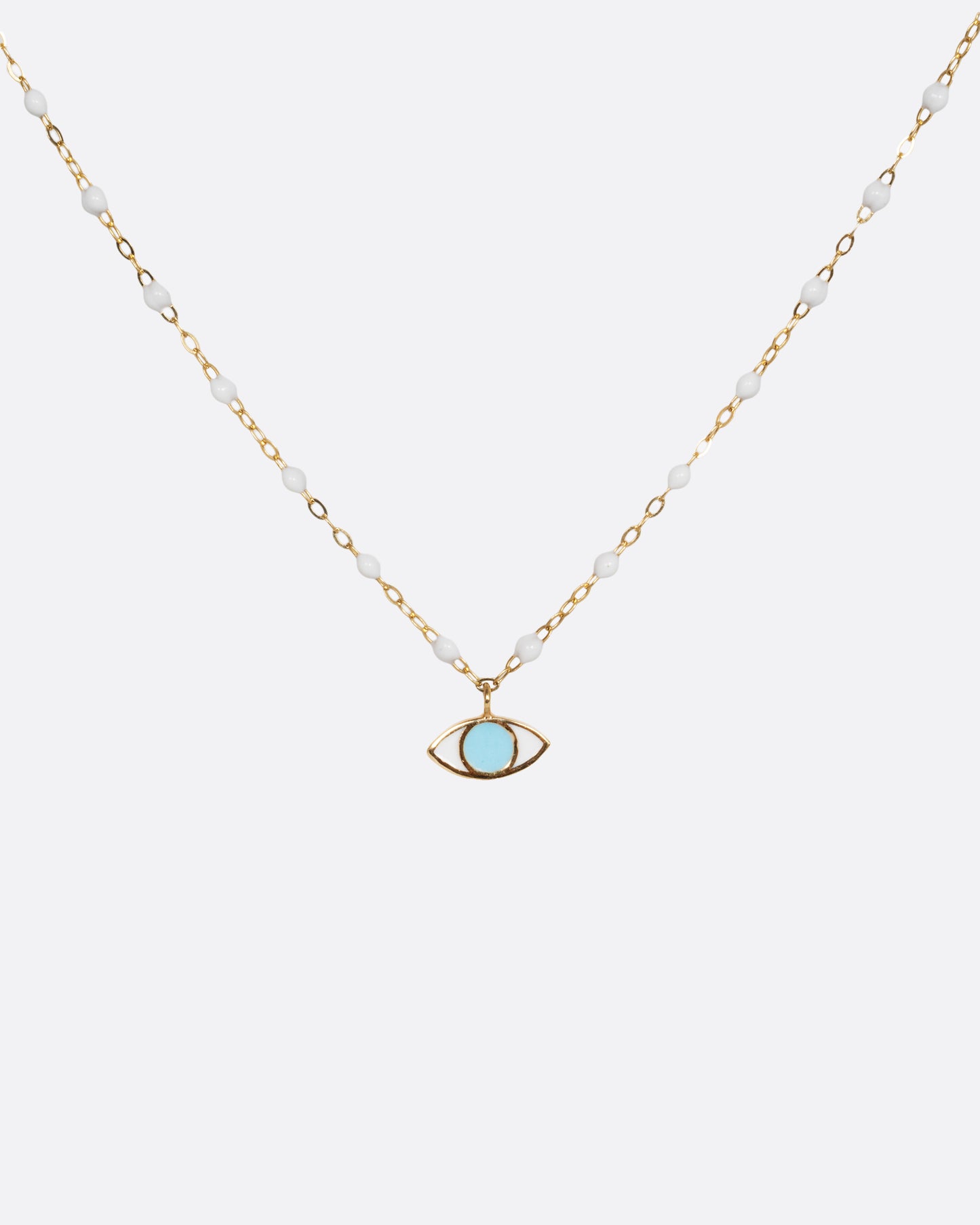 A yellow gold cable chain necklace with droplets of white resin and an eye charm. The iris of the eye charm is turquoise blue enamel and the sclera is white. Shown from the front.