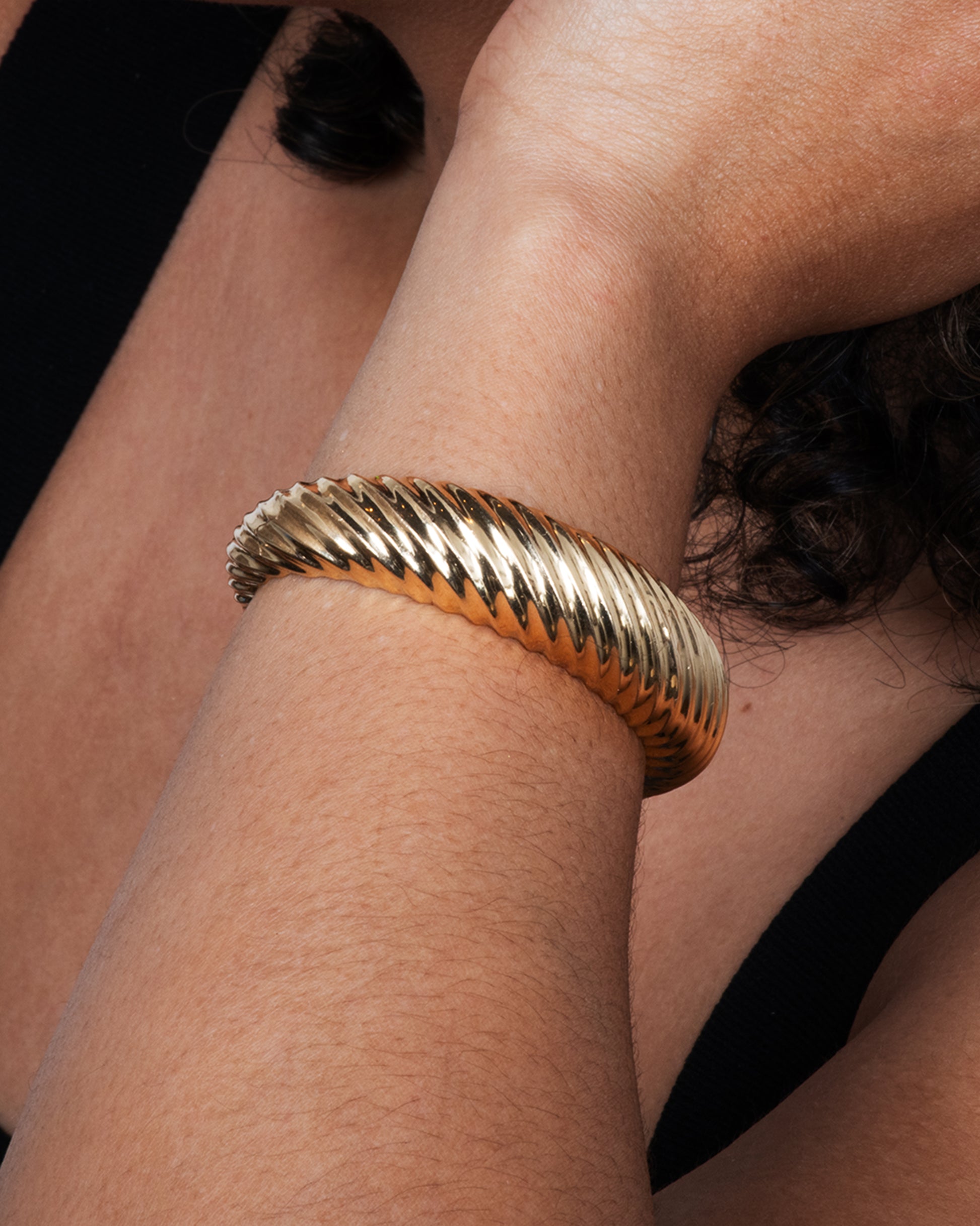 Yellow gold cuff with ridges that create a twisted look. View on a wrist.