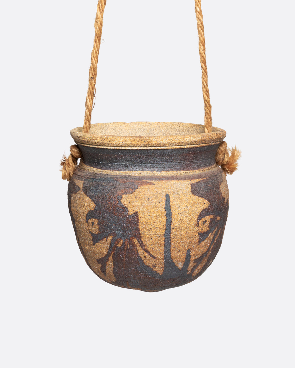 A ceramic pot with an abstract tan and brown pattern and cords for hanging, shown from the front.