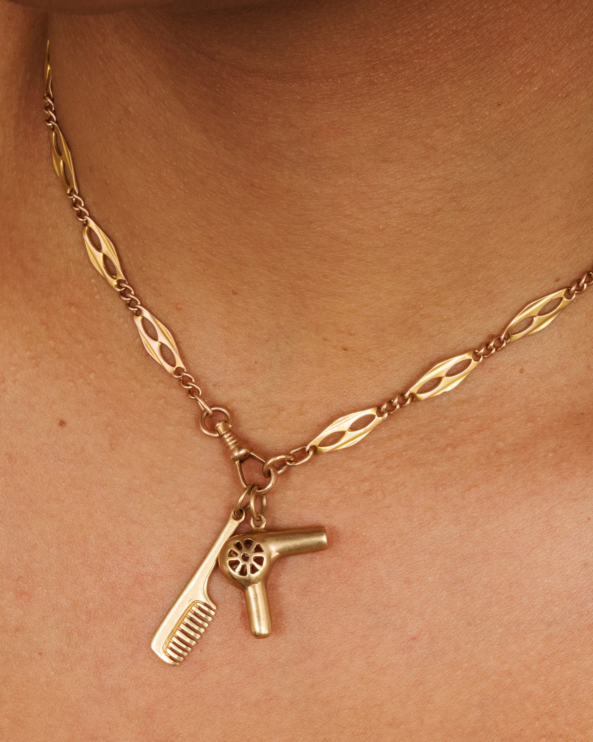 A yellow gold handled comb charm. Shown worn on a watch chain paired with a blowdryer charm.