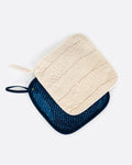 A pair of pot holders- one cream and one indigo blue. Both have contrast stitching. Shown from the front stacked.