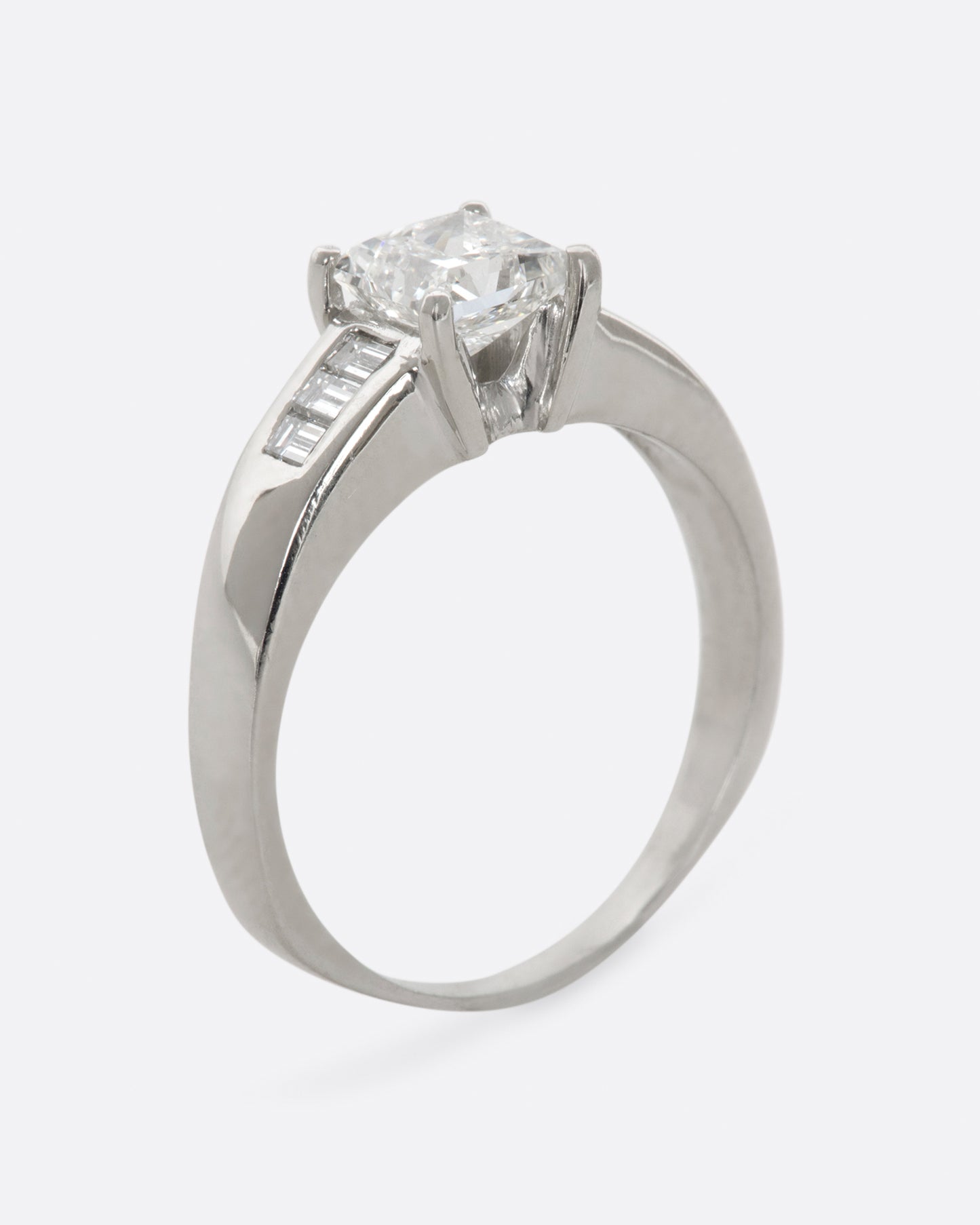 A platinum ring with a prong set princess cut center diamond and three baguette diamonds on either side. View standing up.