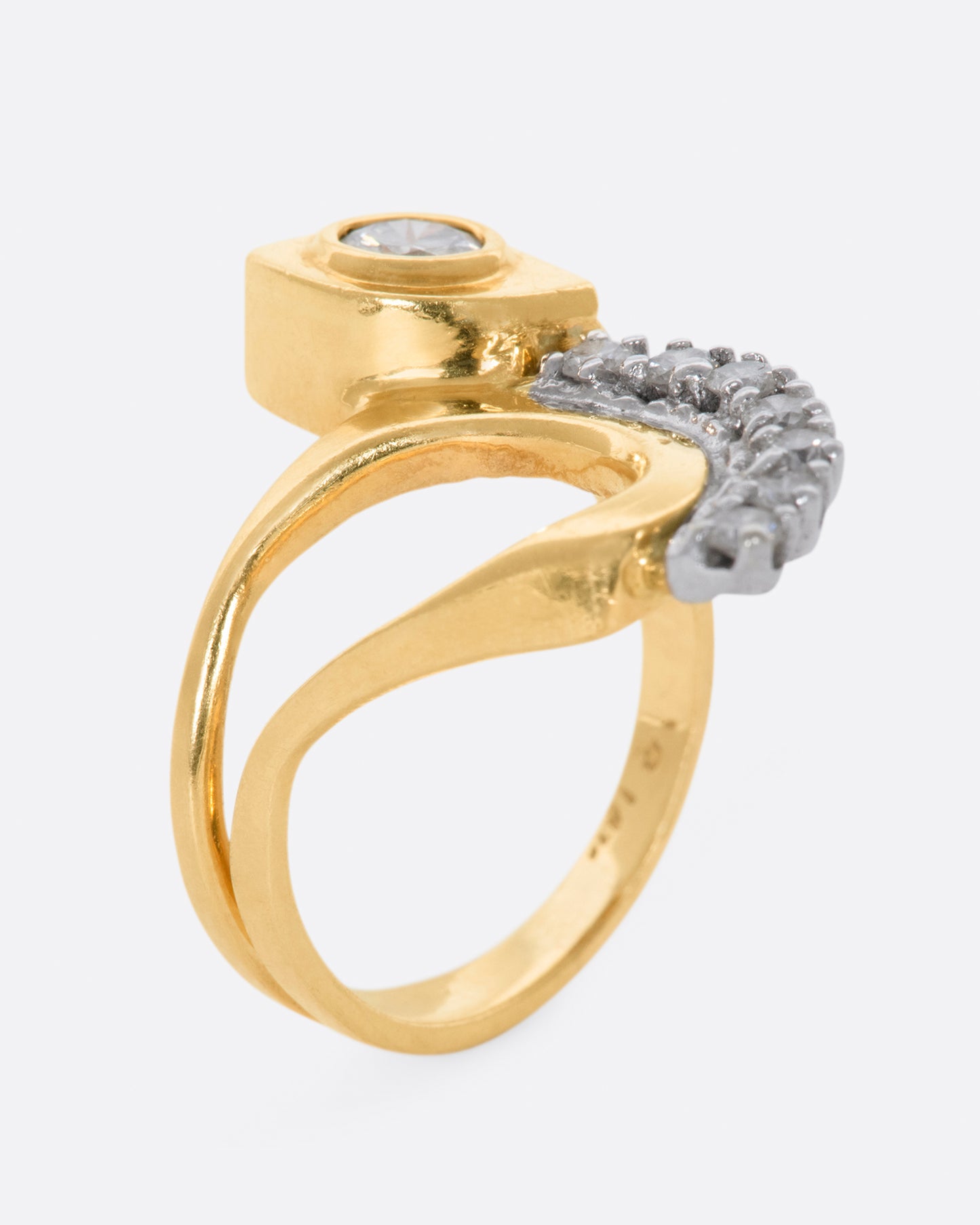 Yellow gold abstract ring with one bezel set round diamond and seven prong set diamonds. View standing up.