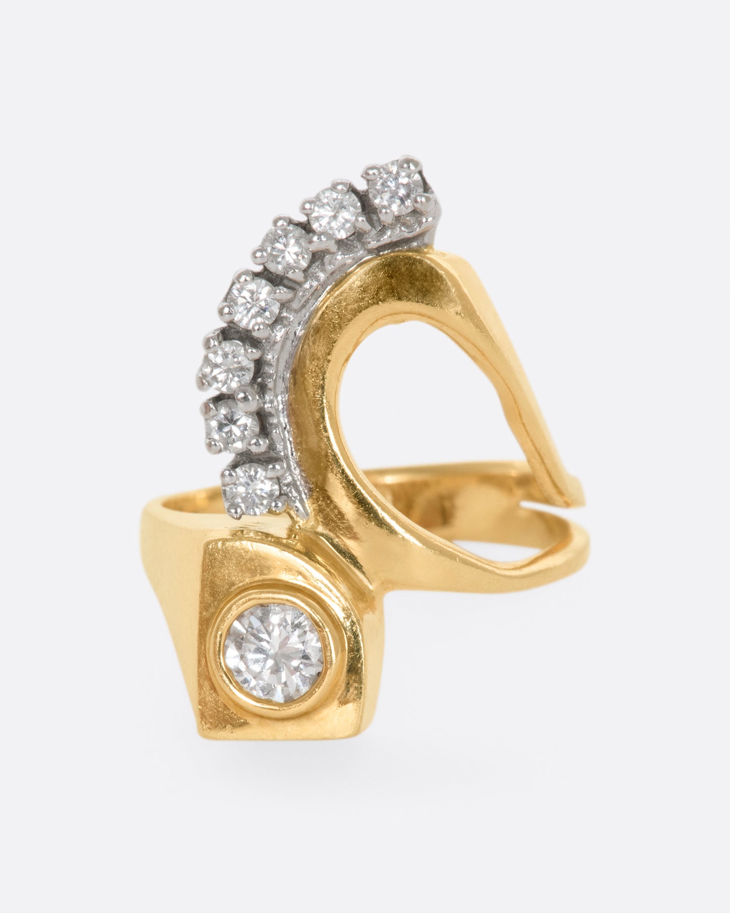 Yellow gold abstract ring with one bezel set round diamond and seven prong set diamonds. View from the front.