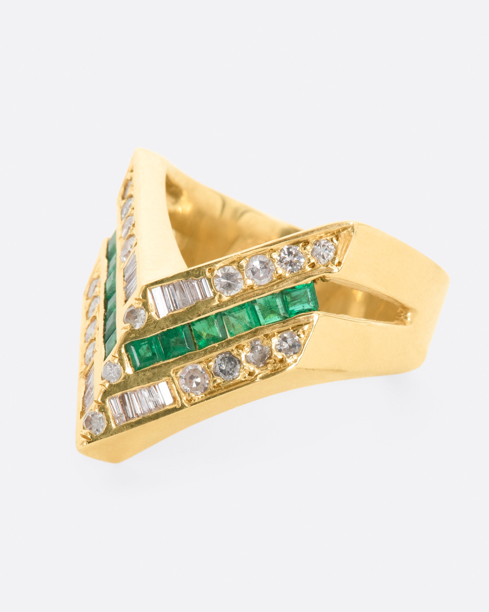 A yellow gold chevron shaped ring with alternating rows of diamonds and emeralds. View from the left side.