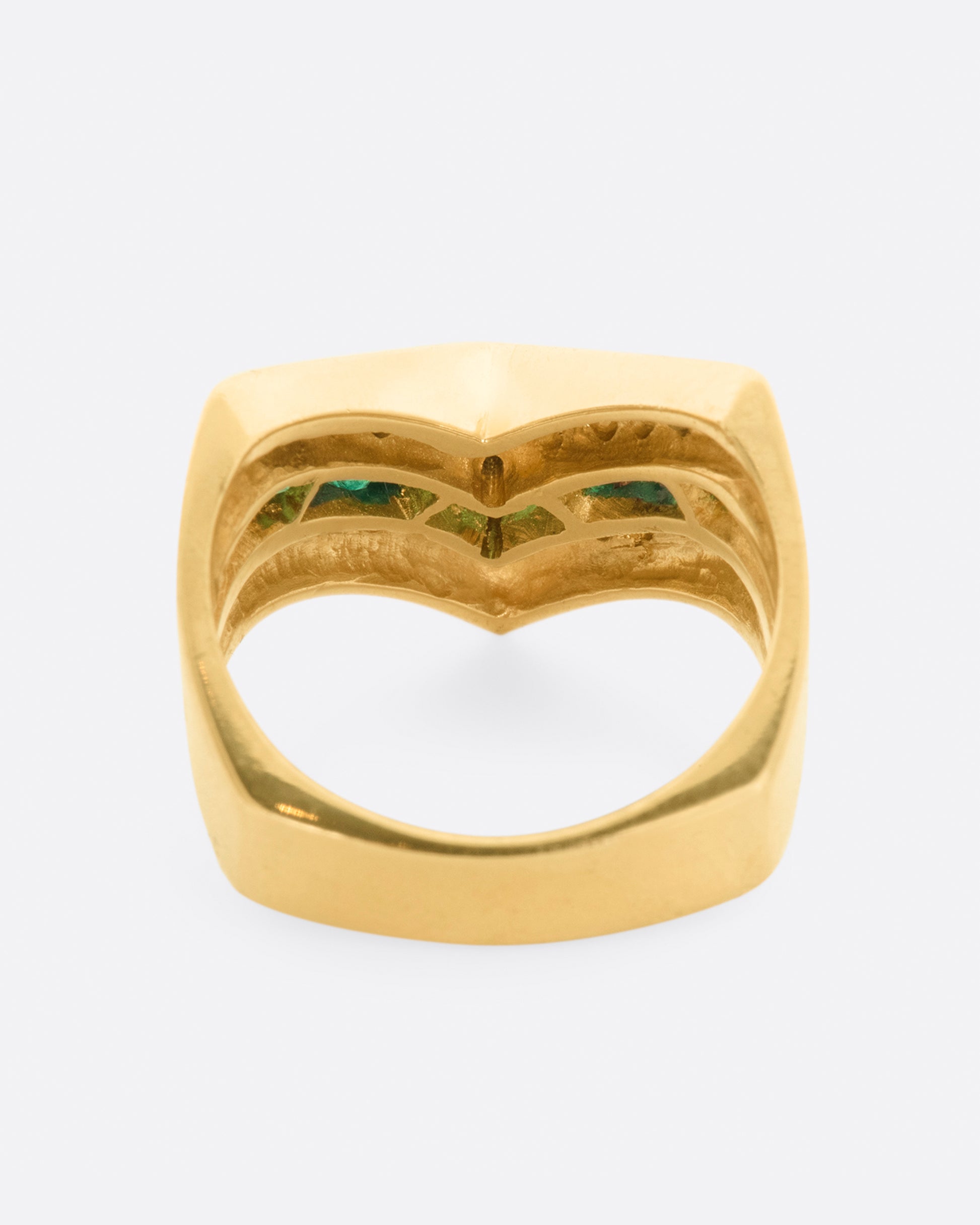 A yellow gold chevron shaped ring with alternating rows of diamonds and emeralds. View from the back.