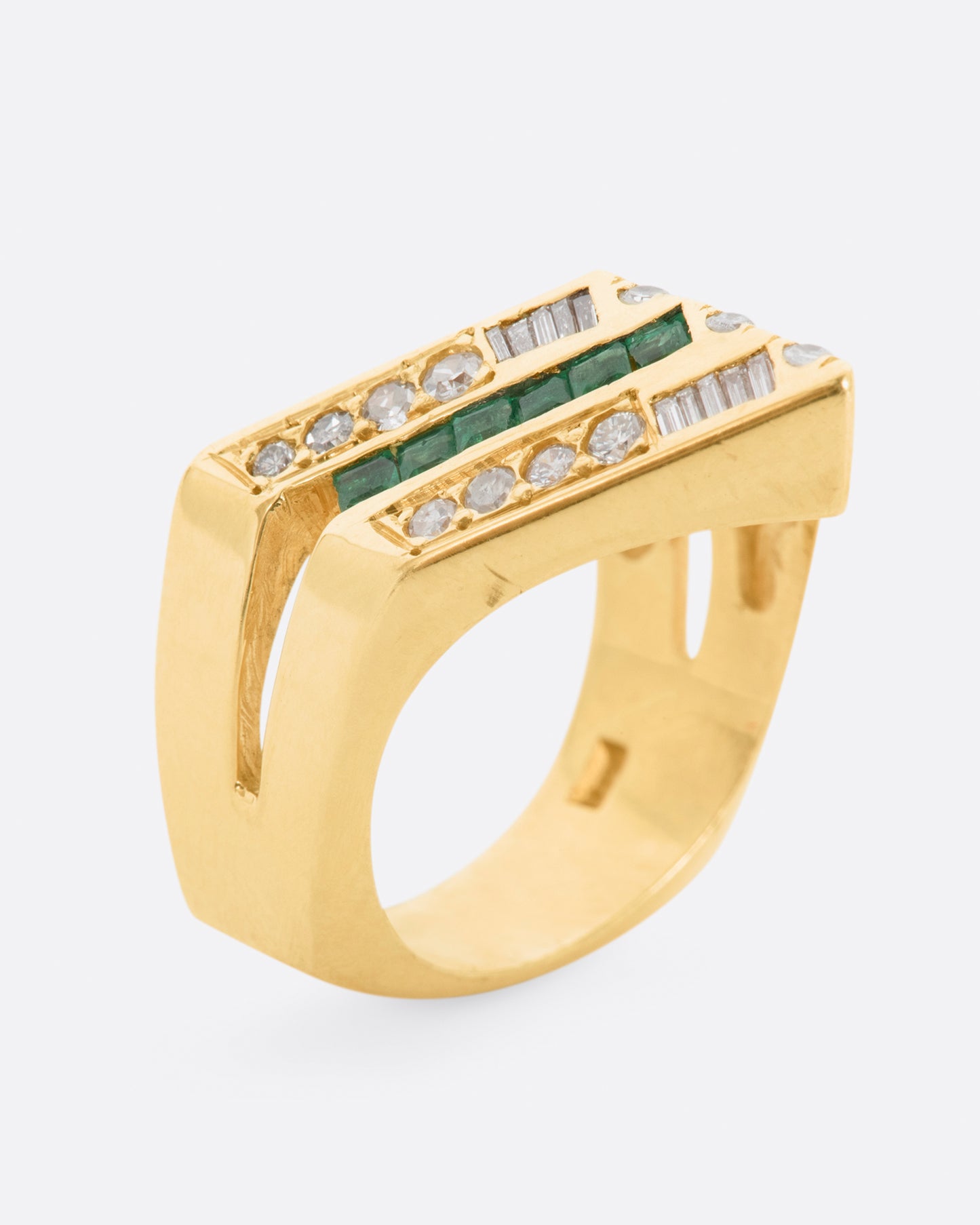 A yellow gold chevron shaped ring with alternating rows of diamonds and emeralds. View standing up.