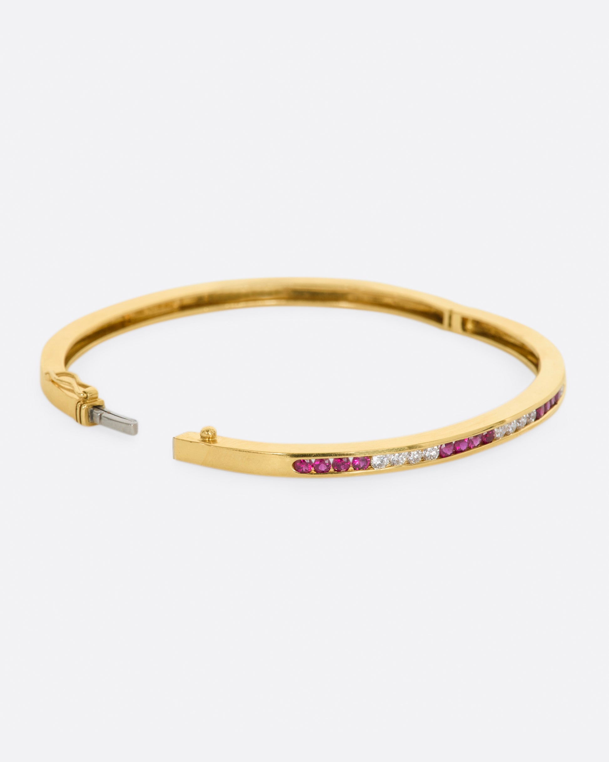 Yellow gold bracelet with alternating sections of channel set rubies and diamonds. View from the side, opened.