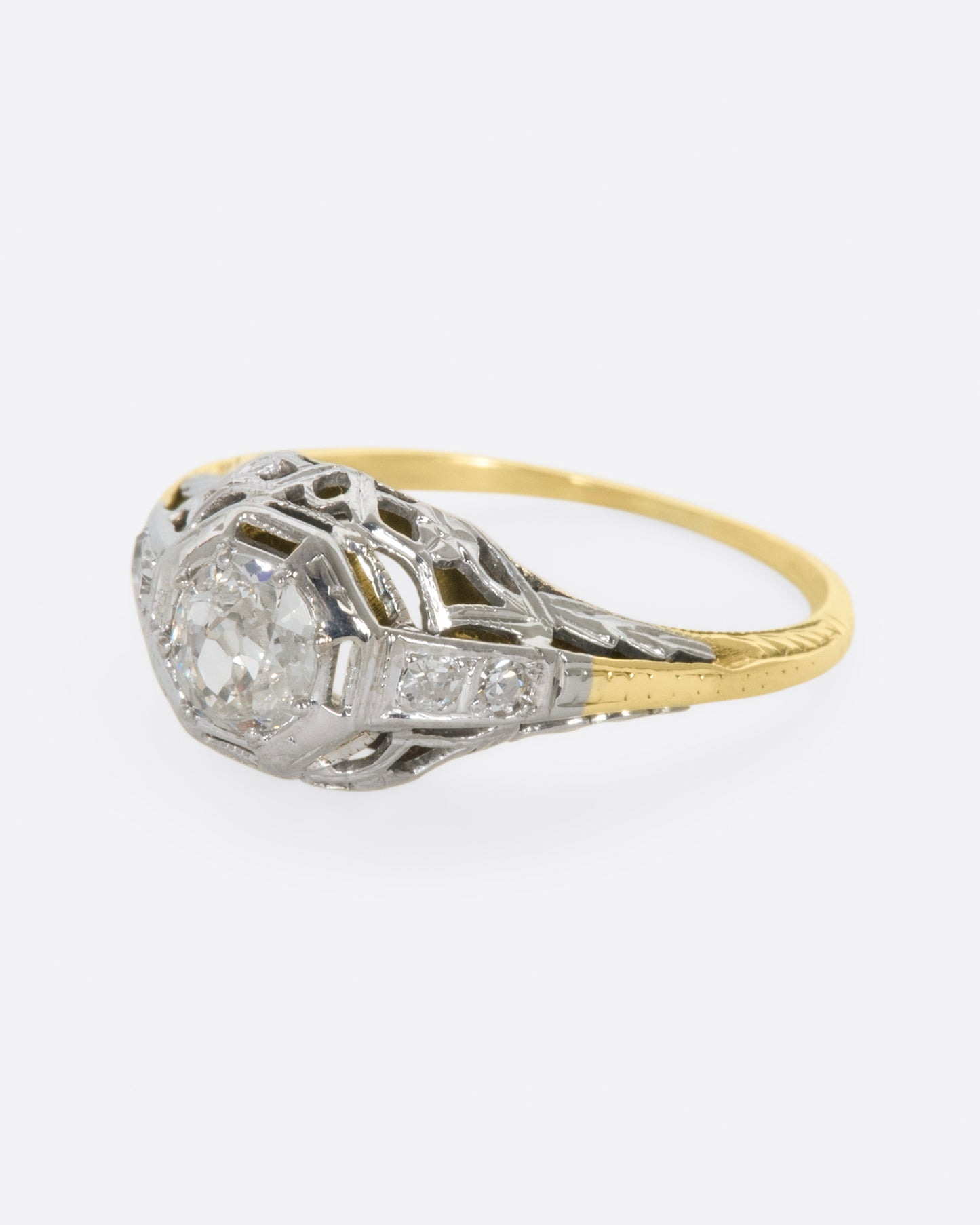 A white gold filigree ring with old mine cut center diamond and a yellow gold band. View from the left side.