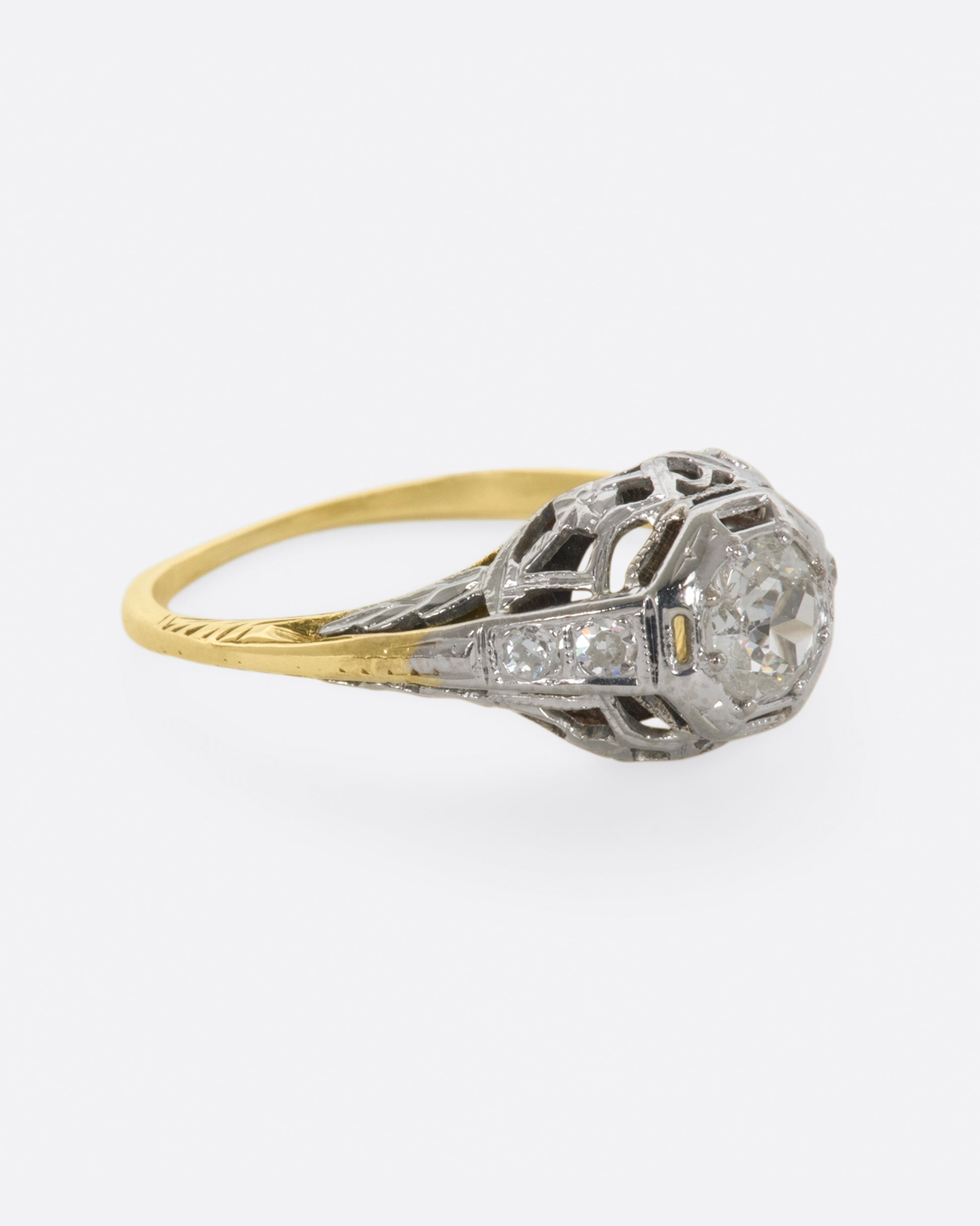 A white gold filigree ring with old mine cut center diamond and a yellow gold band. View from the right side.