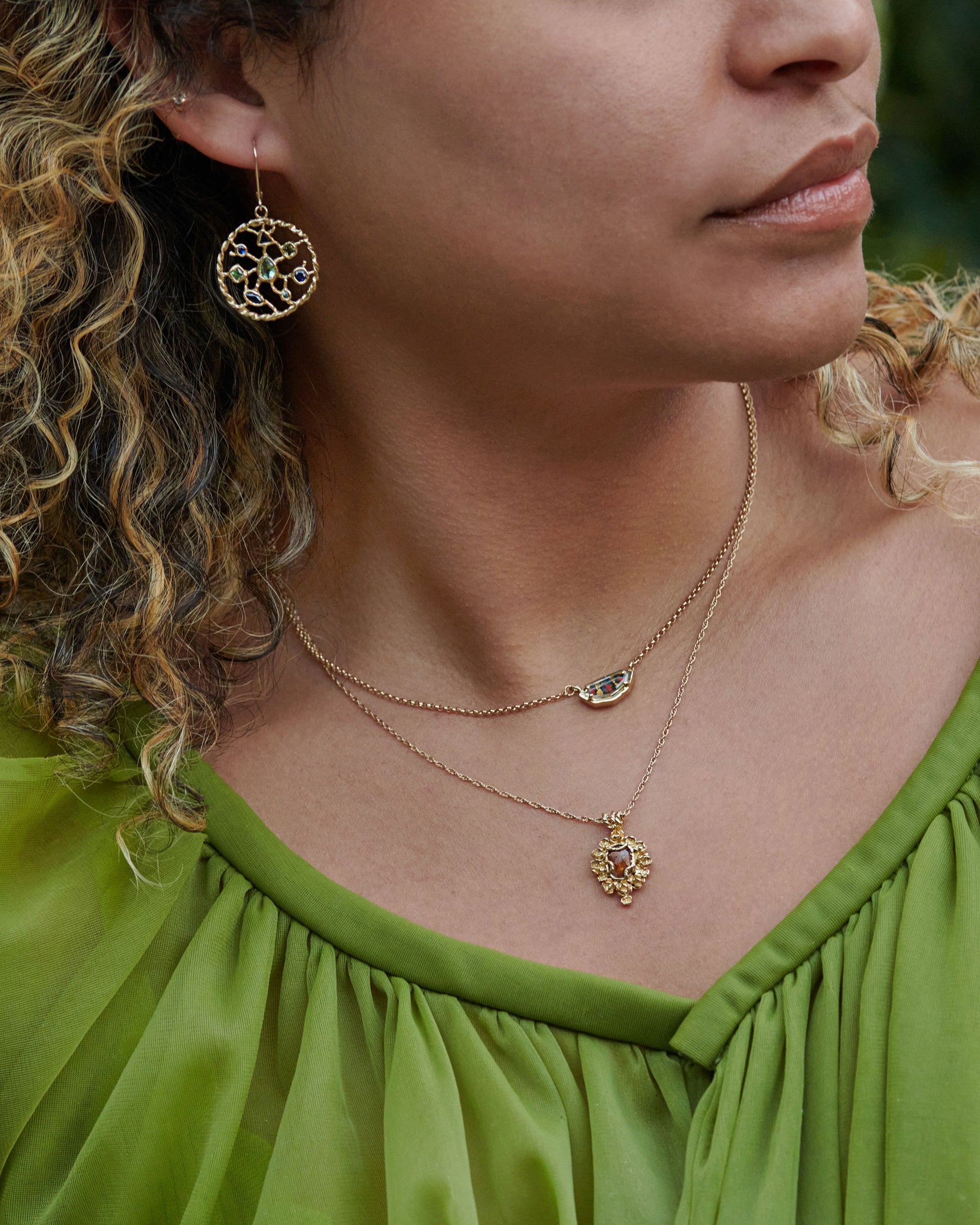 A yellow gold shield shaped necklace with a portrait cut sapphire over micromosaic and goldleaf italian glass and black diamond. View on a person.