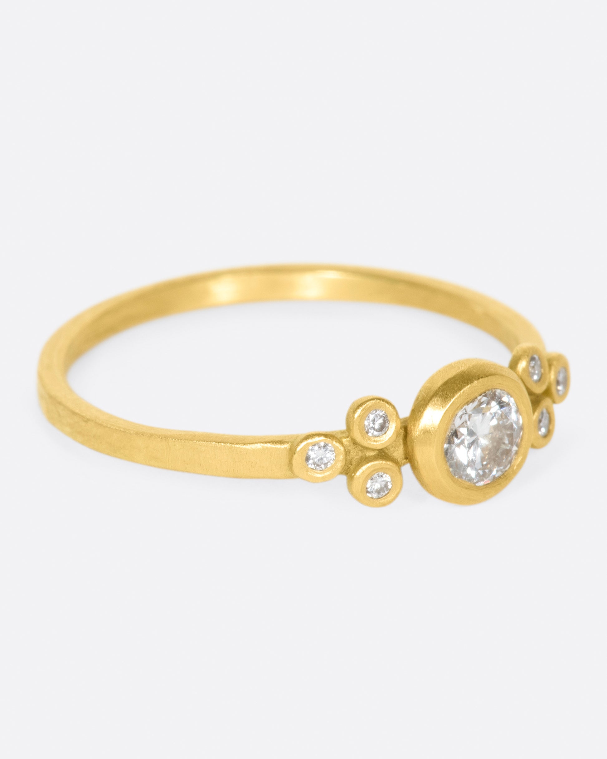 A hammered gold band with a round bezel set diamond at its center, flanked by three smaller round diamonds on either side.