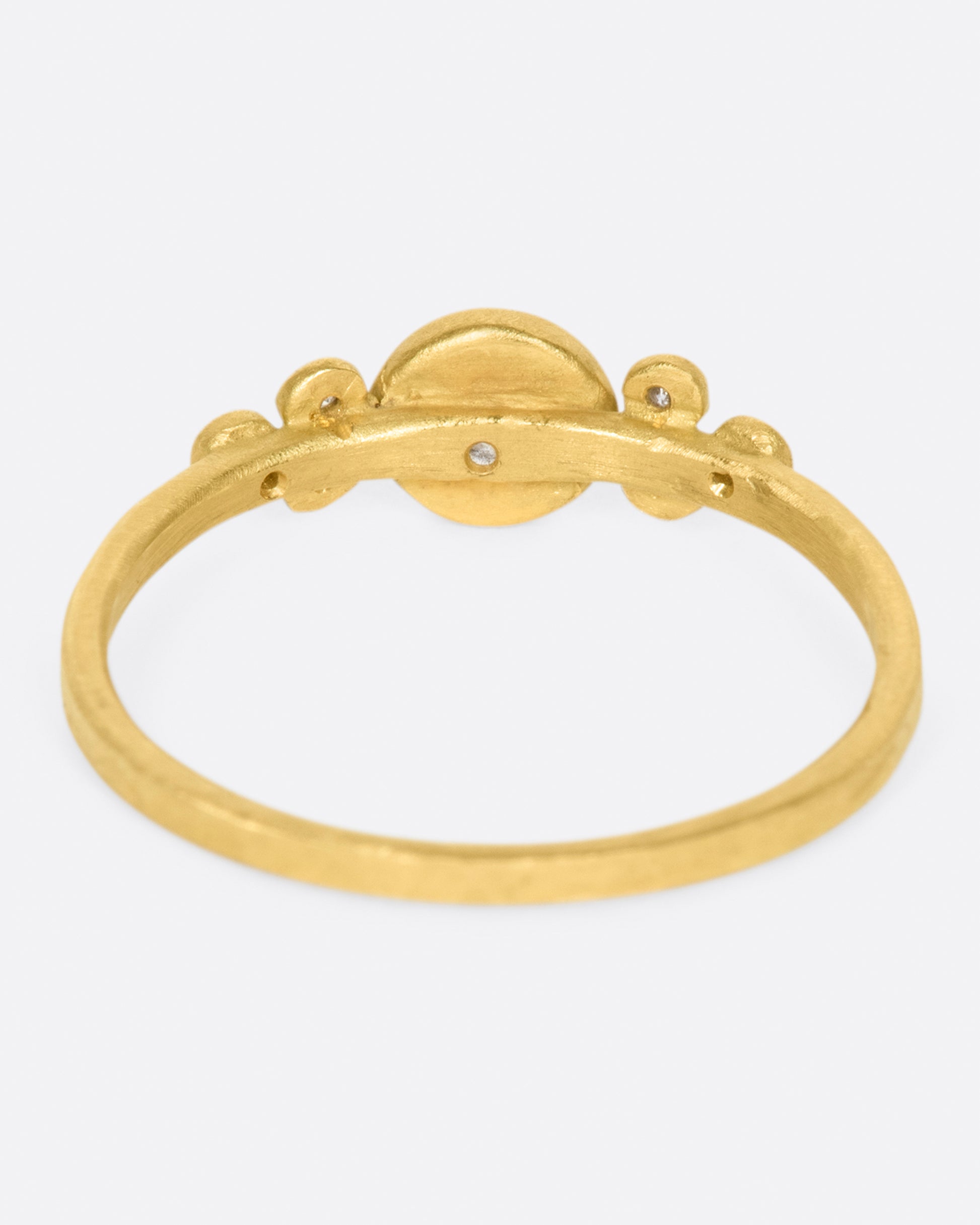 A hammered gold band with a round bezel set diamond at its center, flanked by three smaller round diamonds on either side.