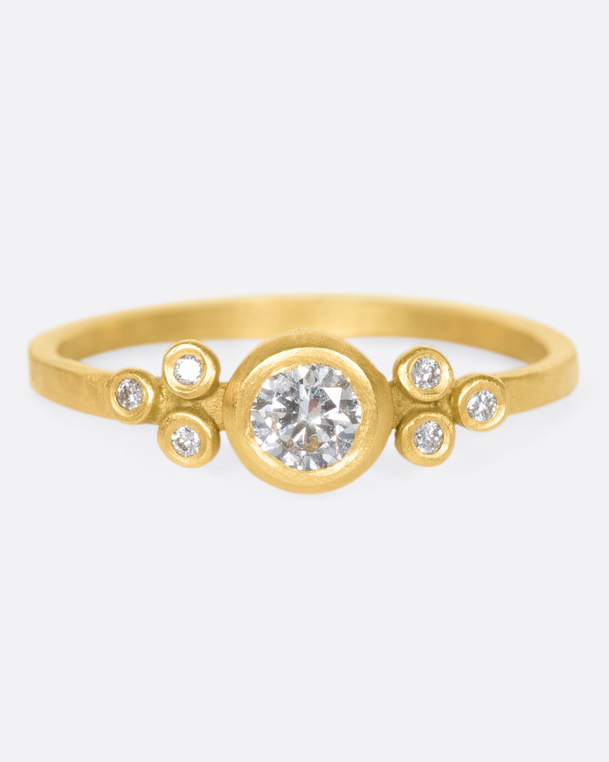 A hammered gold band with a round bezel set diamond at its center, flanked by three smaller round diamonds on either side.