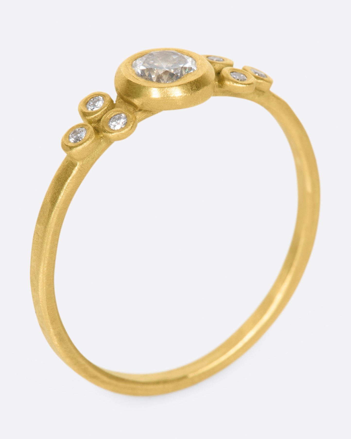 A hammered gold band with a round bezel set diamond at its center, flanked by three smaller round diamonds on either side.