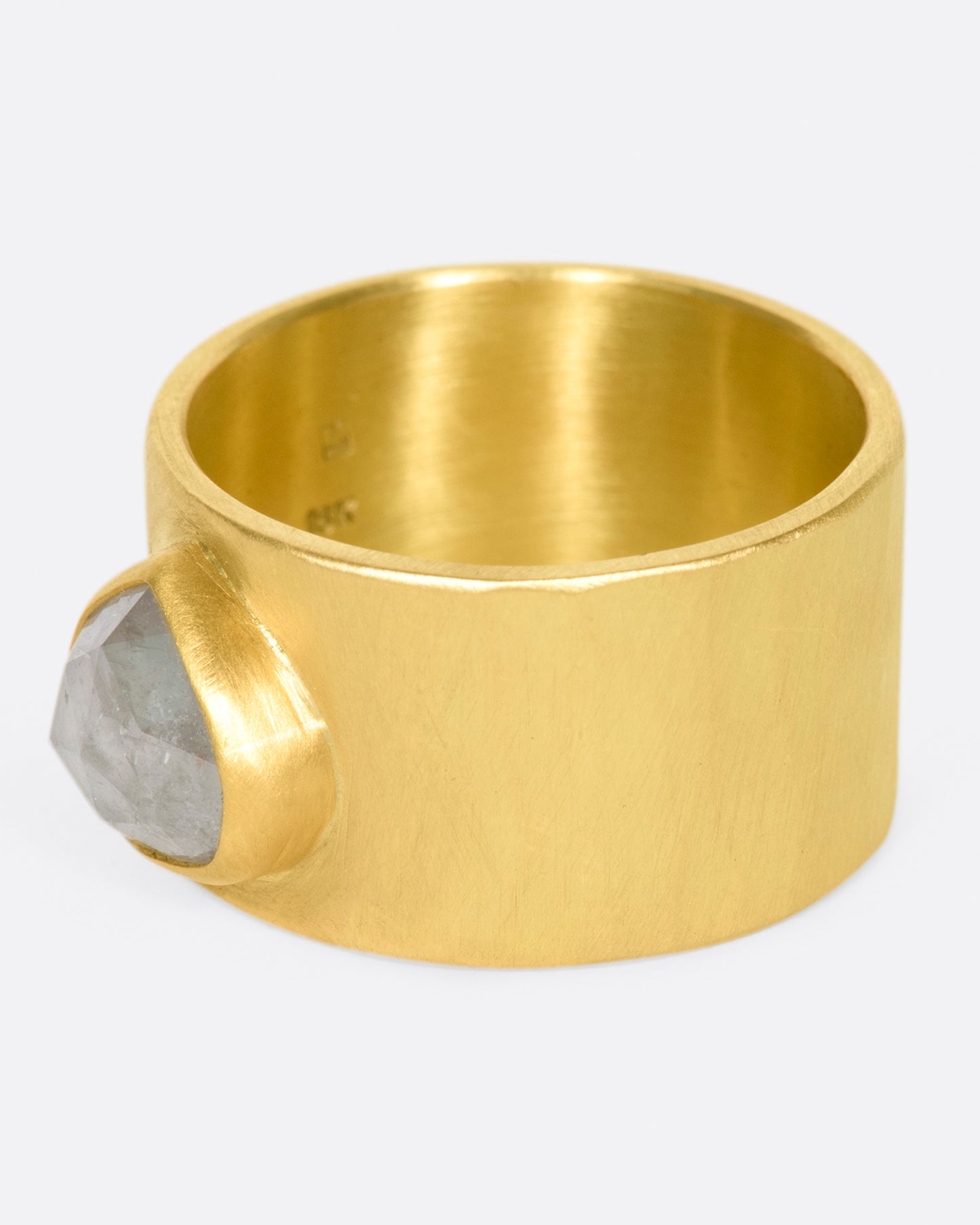 A wide, matte, hammered band with a rose cut gray diamond embedded in a high karat gold setting.