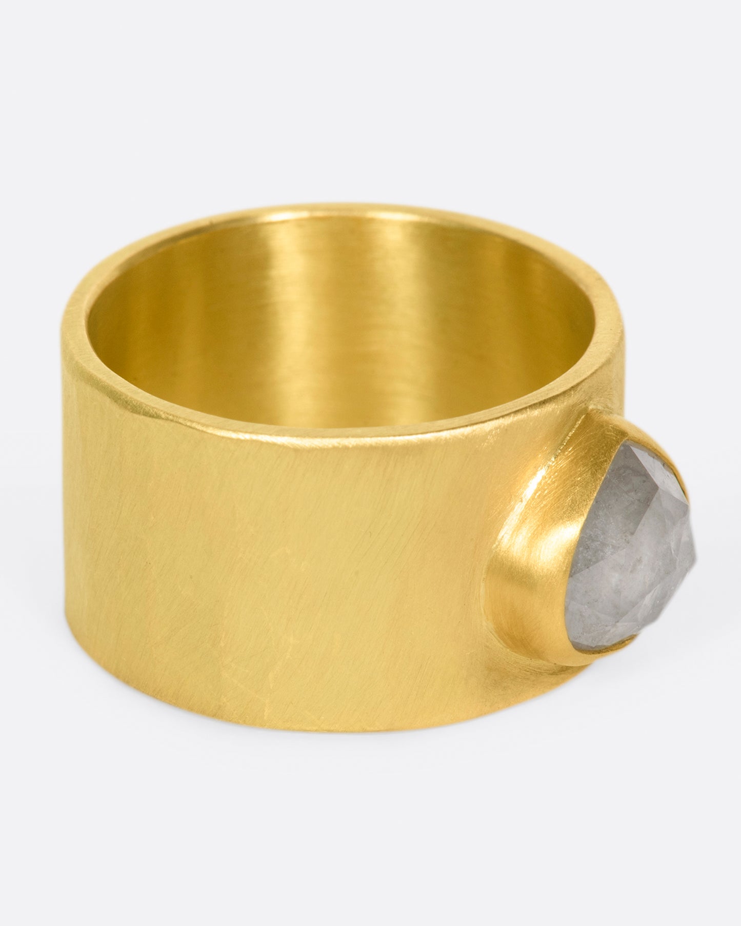 A wide, matte, hammered band with a rose cut gray diamond embedded in a high karat gold setting.