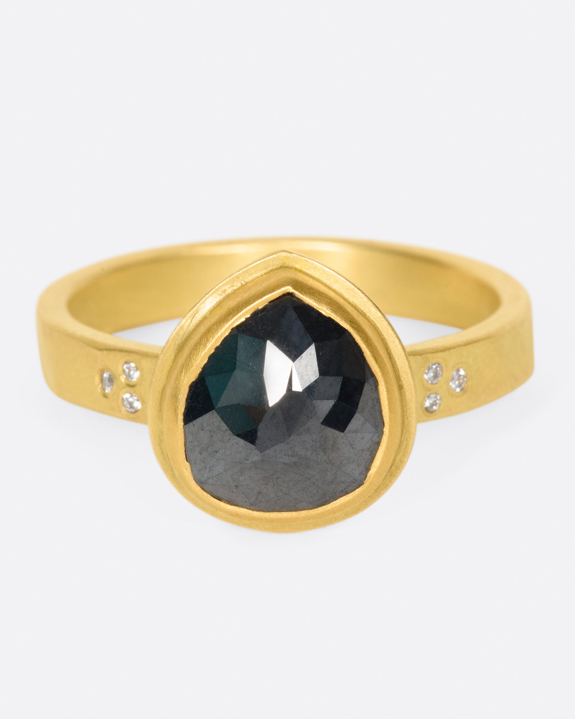 A faceted, pear shaped black diamond in a 22k gold setting with white diamond accents.