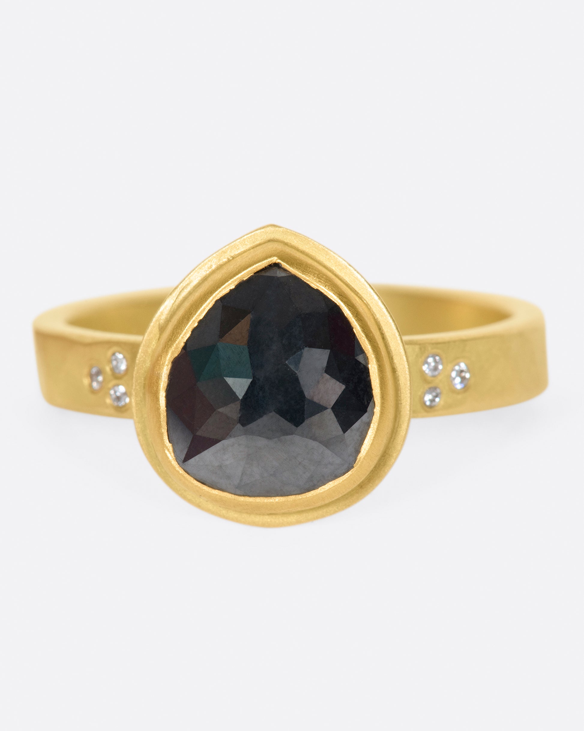 A faceted, pear shaped black diamond in a 22k gold setting with white diamond accents.