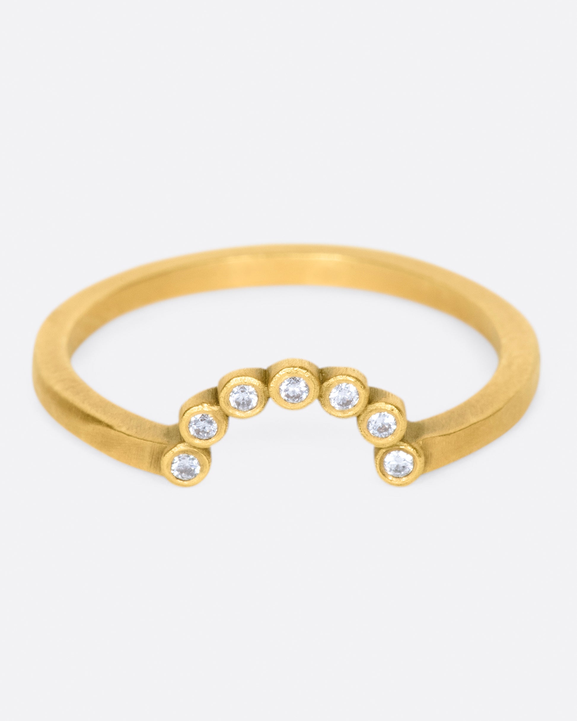 A matte gold ring with an arc of seven bezel set diamonds.