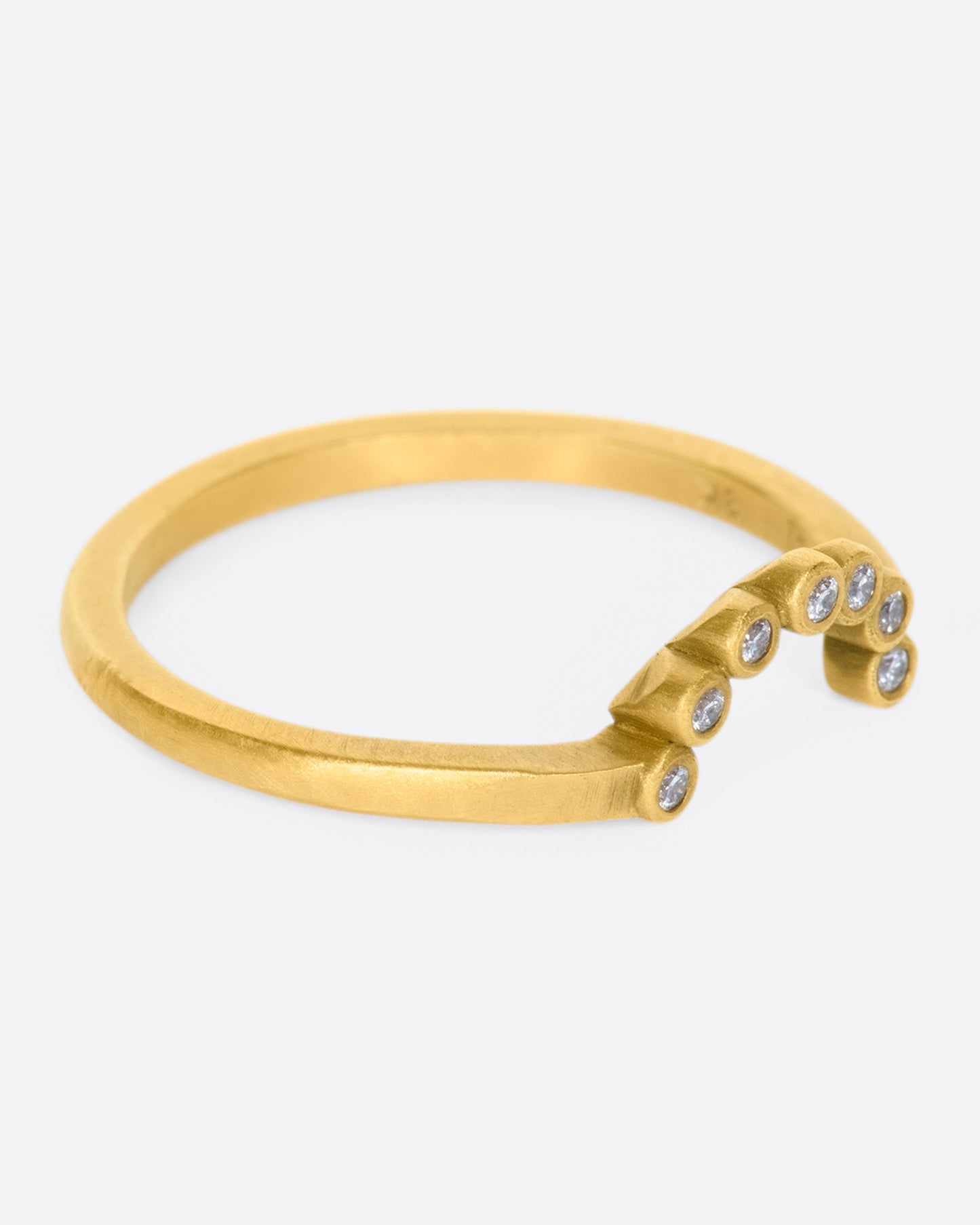 A matte gold ring with an arc of seven bezel set diamonds.