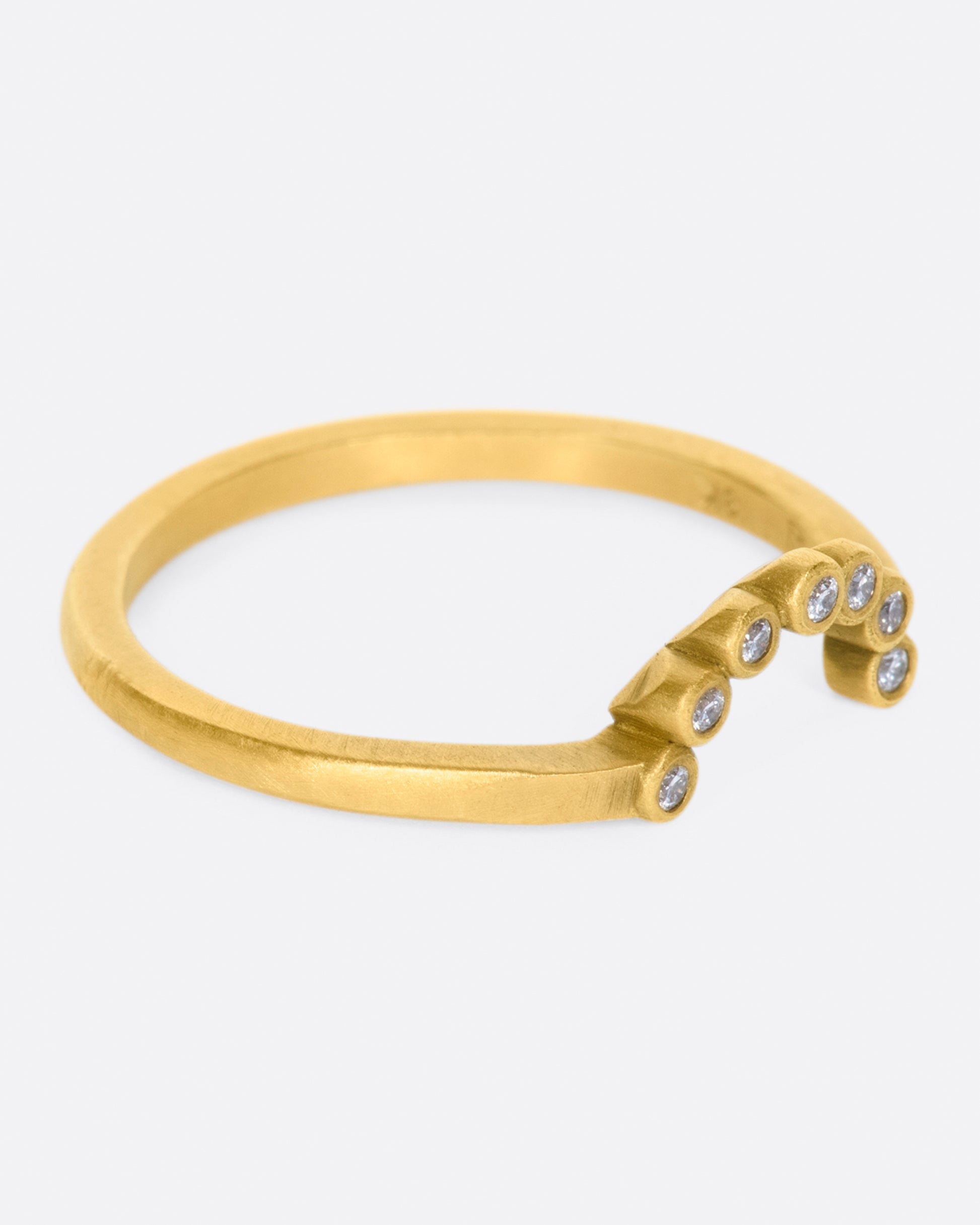 A matte gold ring with an arc of seven bezel set diamonds.