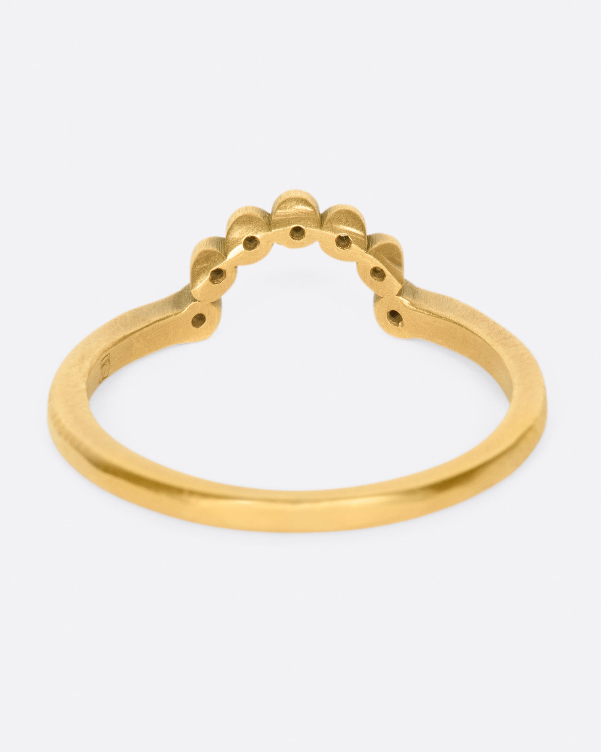 A matte gold ring with an arc of seven bezel set diamonds.