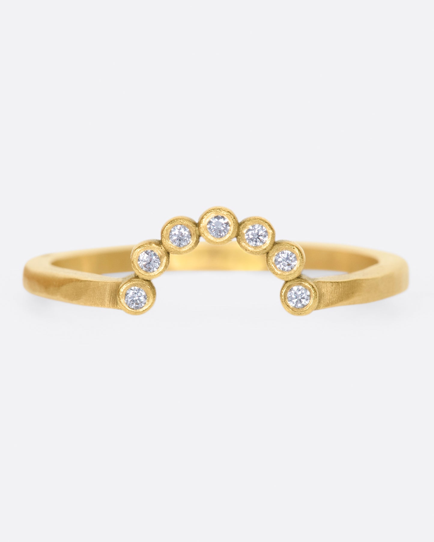 A matte gold ring with an arc of seven bezel set diamonds.