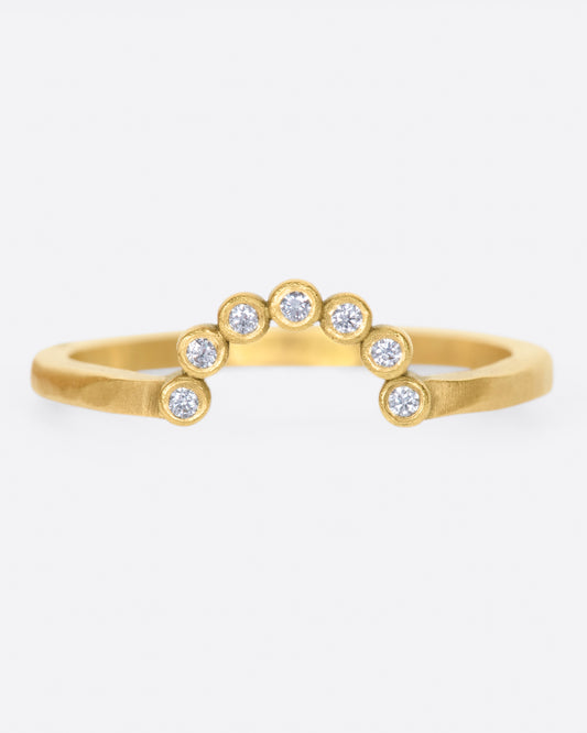 A matte gold ring with an arc of seven bezel set diamonds.