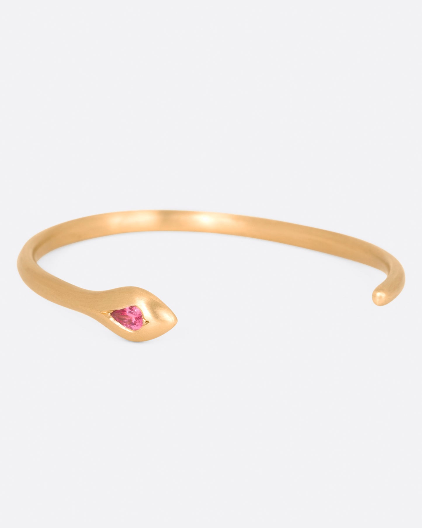 A matte yellow gold snake cuff bracelet with a pear shaped pink sapphire on its head, shown from the side.