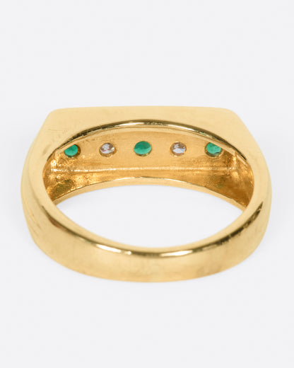 A yellow gold ring with a row of five channel set stones; three emeralds and two diamonds. Shown from the back.