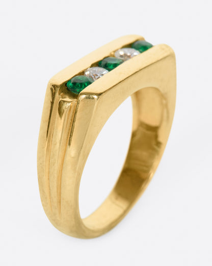 A yellow gold ring with a row of five channel set stones; three emeralds and two diamonds. Shown from the side standing up.
